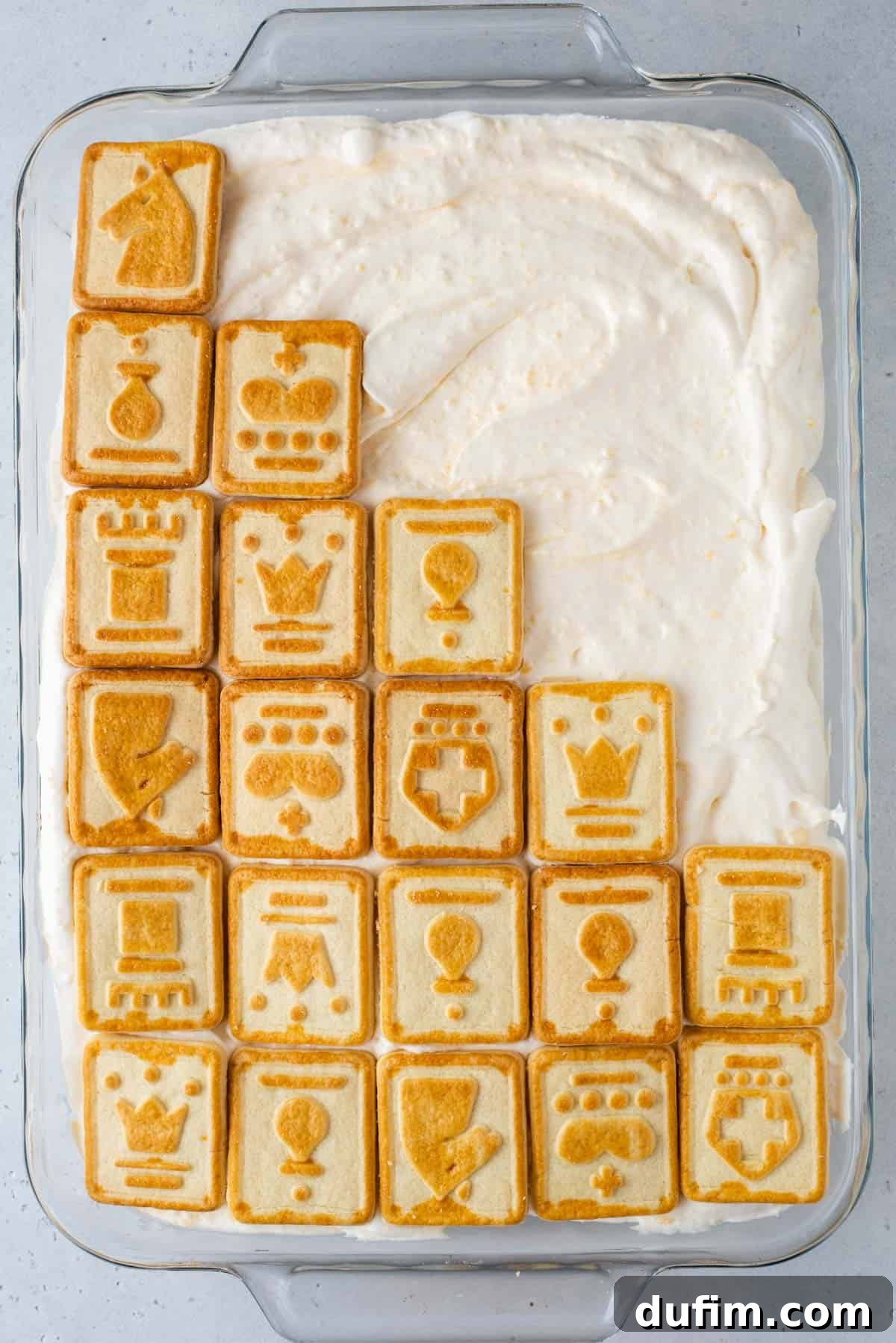 Paula Deen banana pudding in a clear glass dish, with Chessmen cookies arranged on top of one half of the dessert, ready for serving.