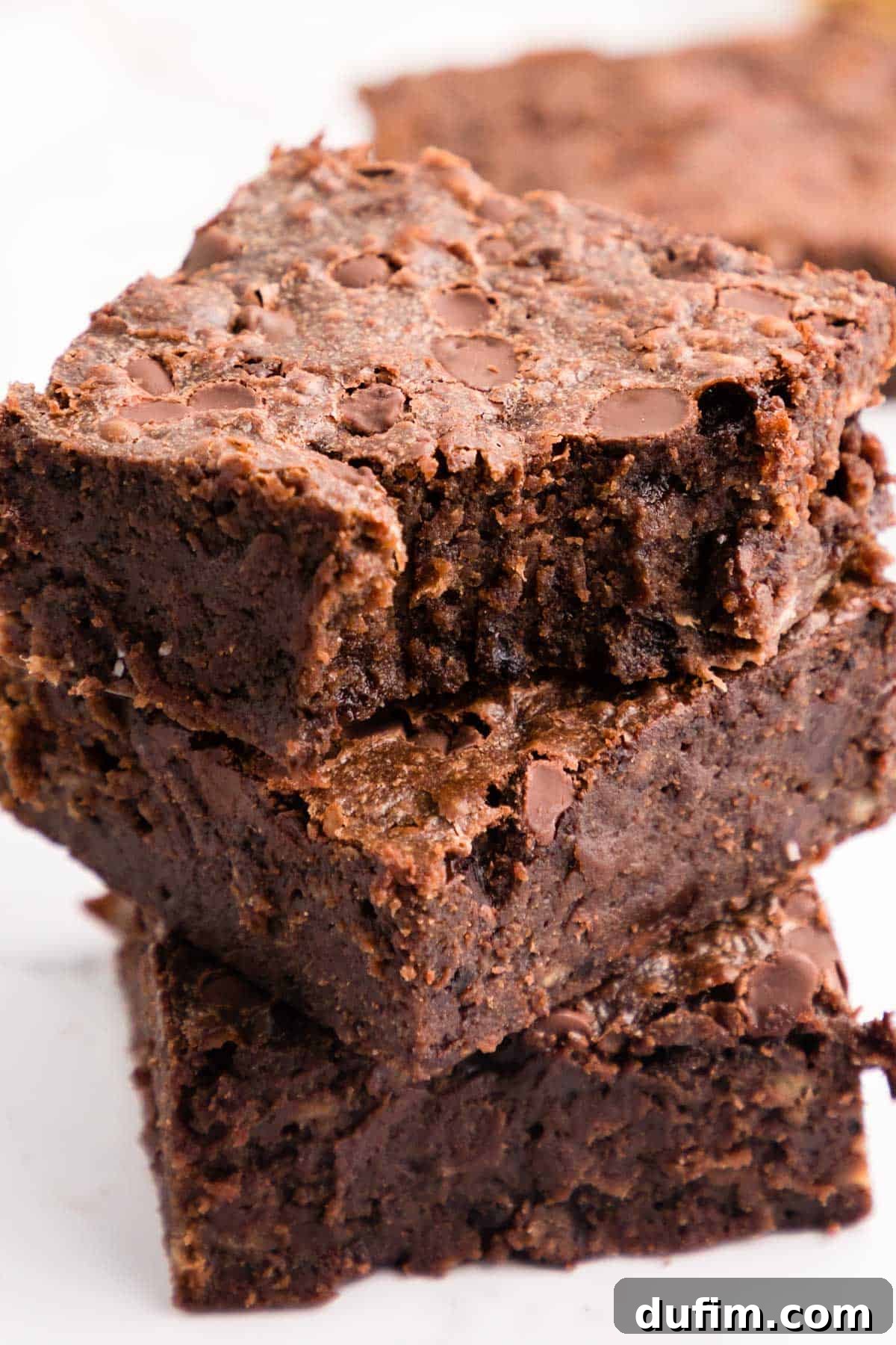 A stack of three banana brownies, with a bite out of the one on top, showcasing their fudgy texture and chocolate chips.
