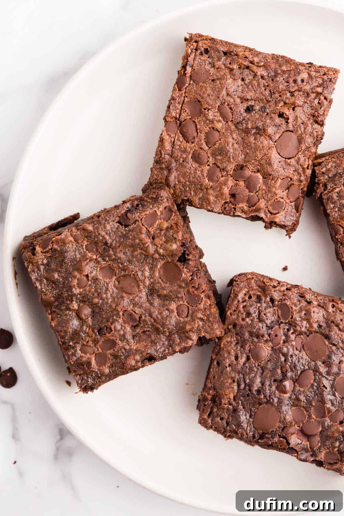 Four perfectly arranged fudgy banana brownies on a pristine white plate, showcasing their inviting texture and generous chocolate chips.