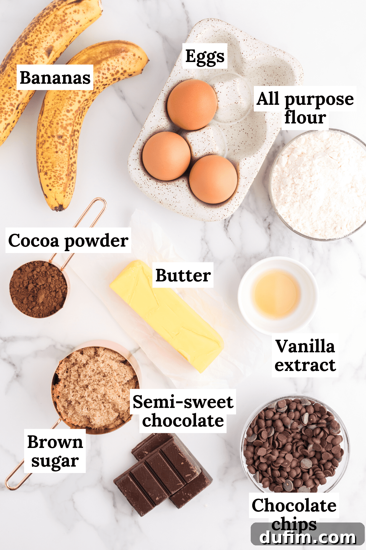 A beautiful arrangement of all the ingredients needed for banana brownies: a bowl of vibrant chocolate chips, semi-sweet chocolate bars, golden brown sugar, clear vanilla extract, creamy butter, ripe bananas, fresh eggs, all-purpose flour, and rich cocoa powder.