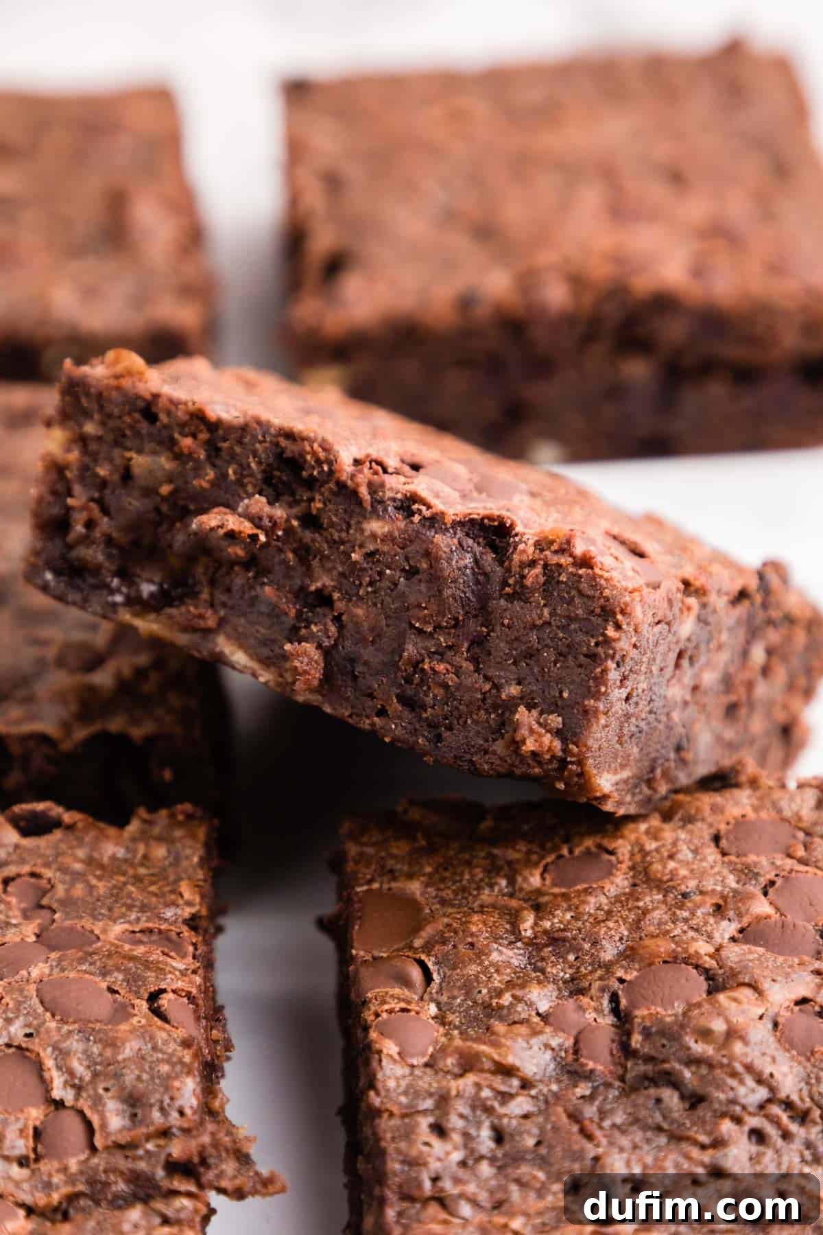 An inviting arrangement of fudgy banana brownies, some whole and some with a bite taken, highlighting their rich chocolatey and moist texture, set against a warm, inviting backdrop.
