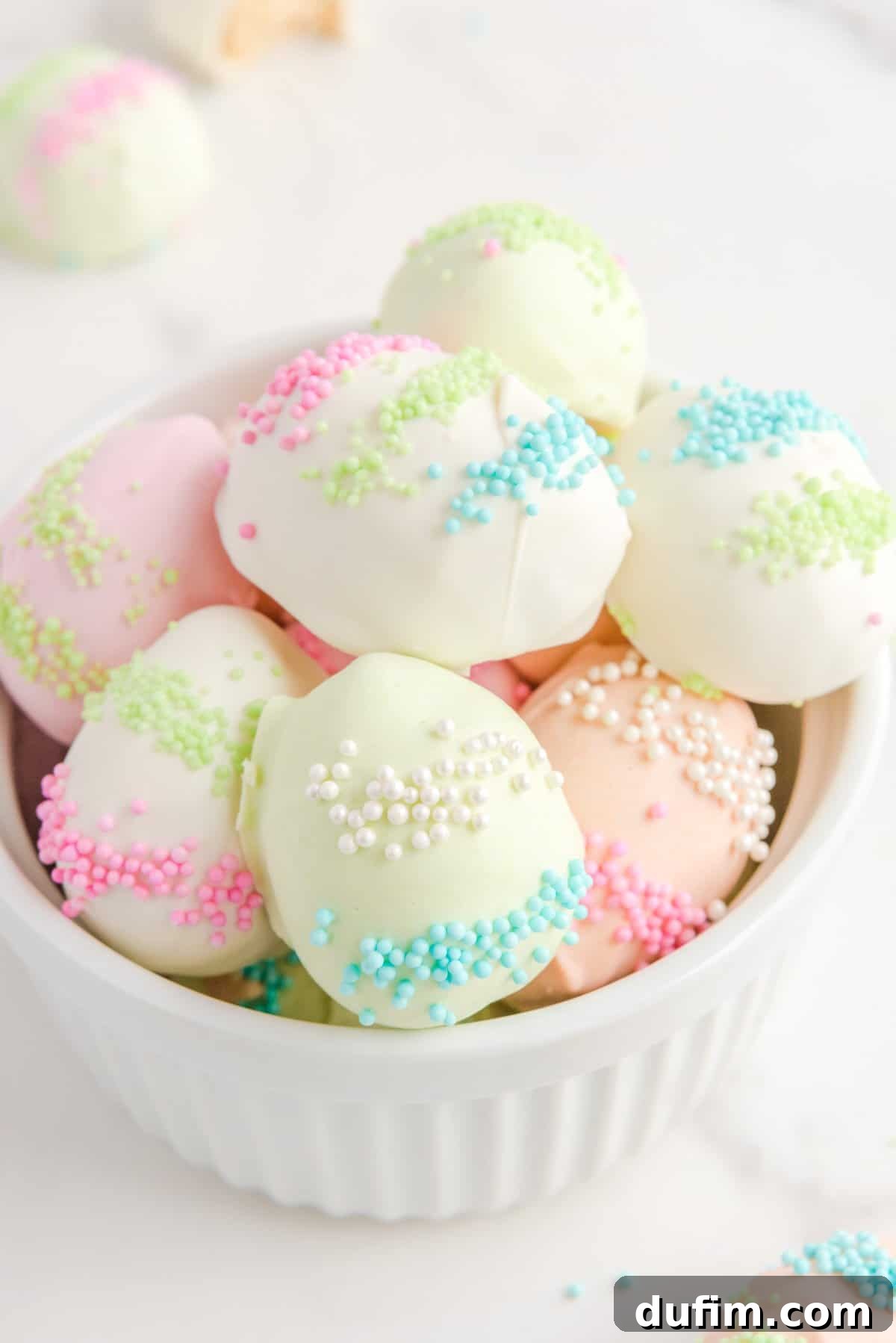 a pile of easter egg truffles in a white bowl on a counter top, with more truffles around it