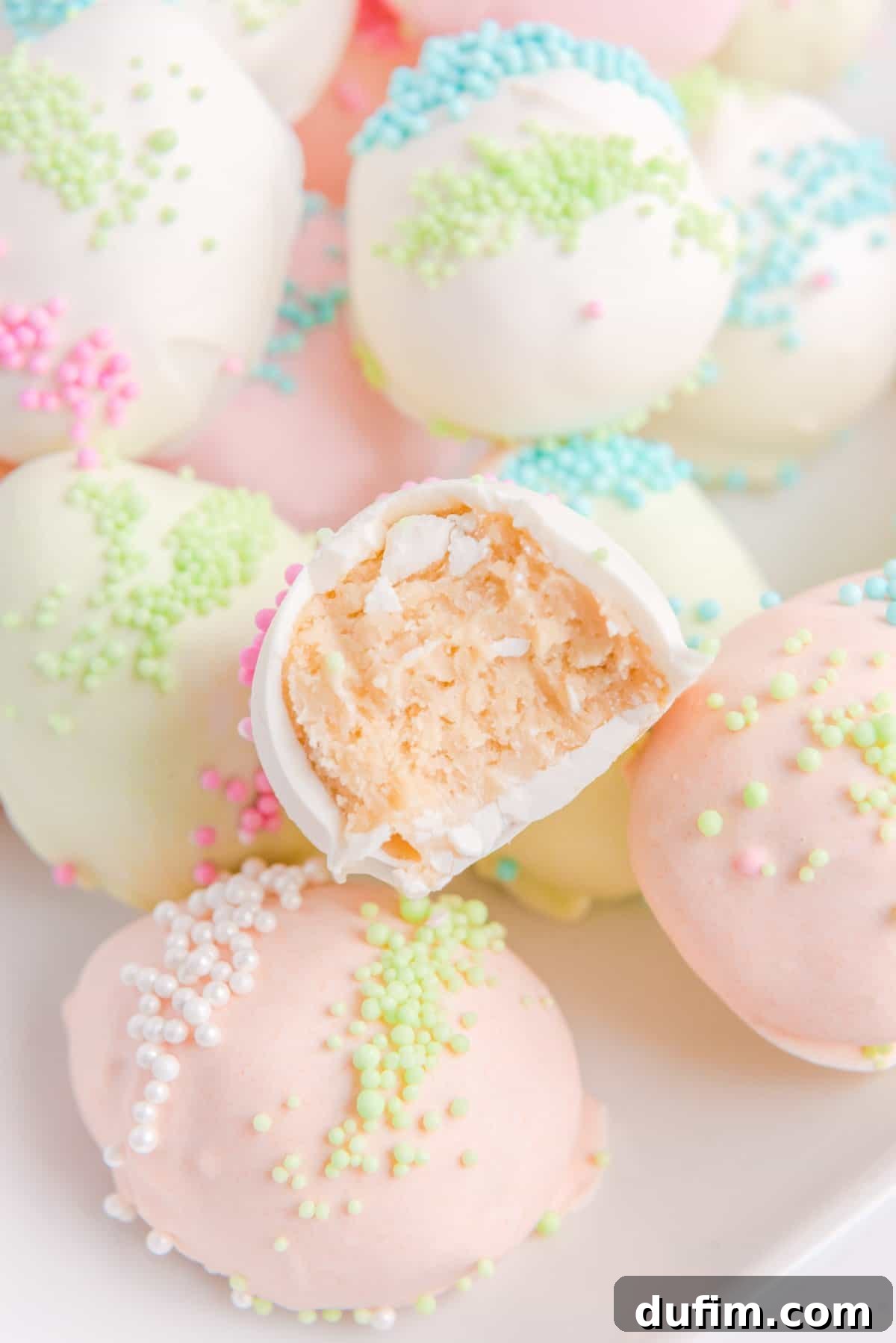 a pile of pink and white easter egg truffles with sprinkles on them, with one half eaten truffle on top