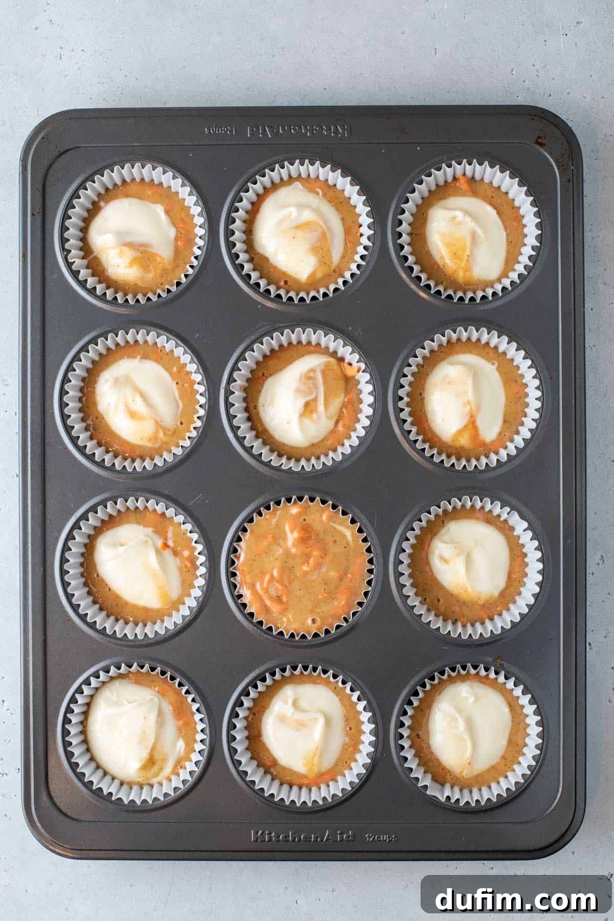 Irresistible Carrot Muffins 10 A muffin pan filled with paper lines and carrot cake muffin batter with cream cheese filling