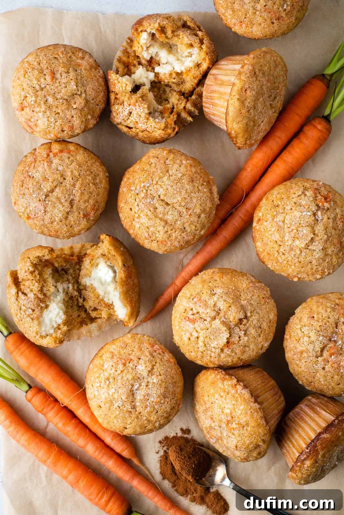 Irresistible Carrot Muffins 12 Carrot cake muffins arranged around carrots, a spoon of spices, and one muffin broken open to reveal the cream cheese filling inside