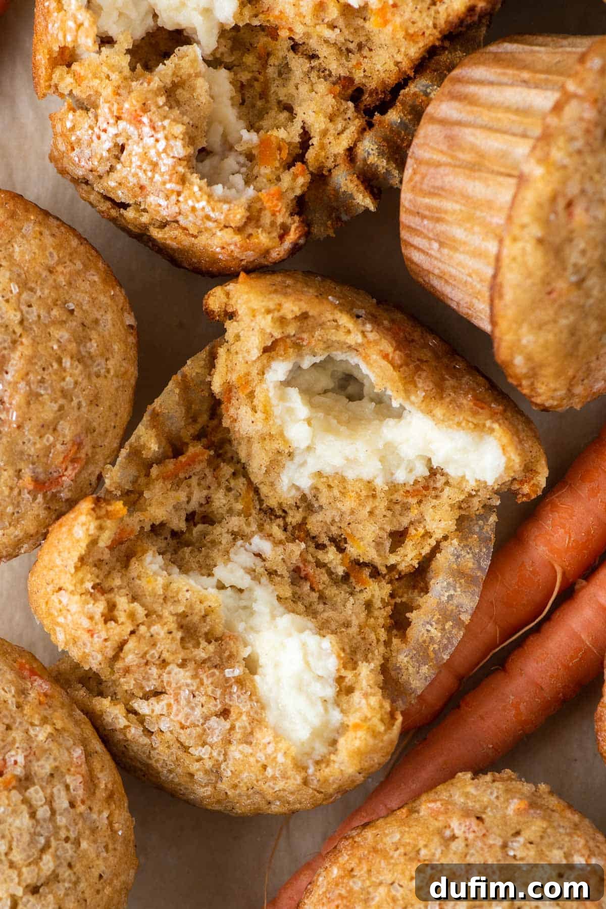 Irresistible Carrot Muffins 4 Carrot cake muffins arranged around carrots, a spoon of spices, and one muffin broken open to reveal the cream cheese filling inside