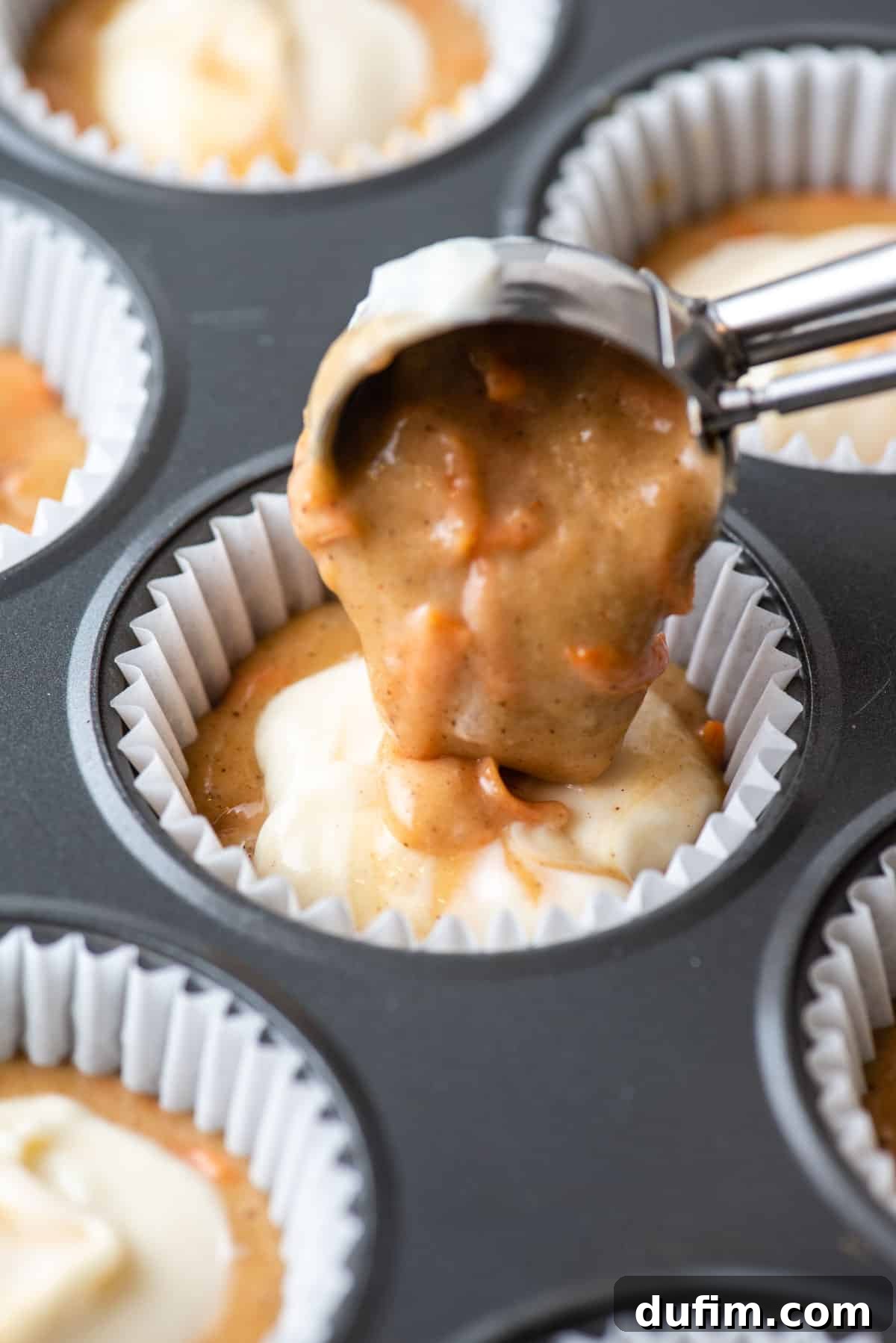 Irresistible Carrot Muffins 8 Carrot cake muffin batter being placed as the top layer in a paper liner with more batter and cream cheese filling already in it.
