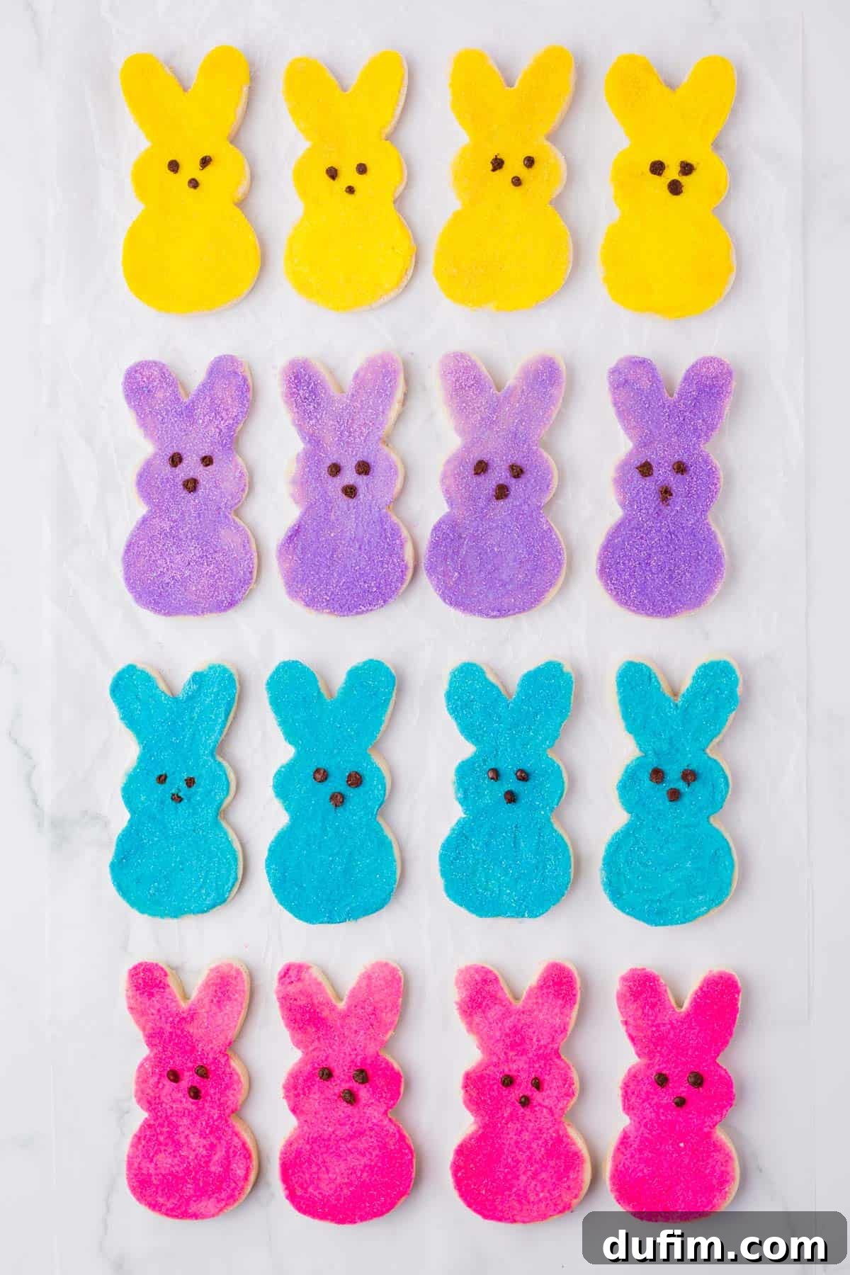 Festive Peeps Bunny Sugar Cookies 4 rows of yellow, blue, purple and pink peeps bunny cookies lined up on a countertop surface