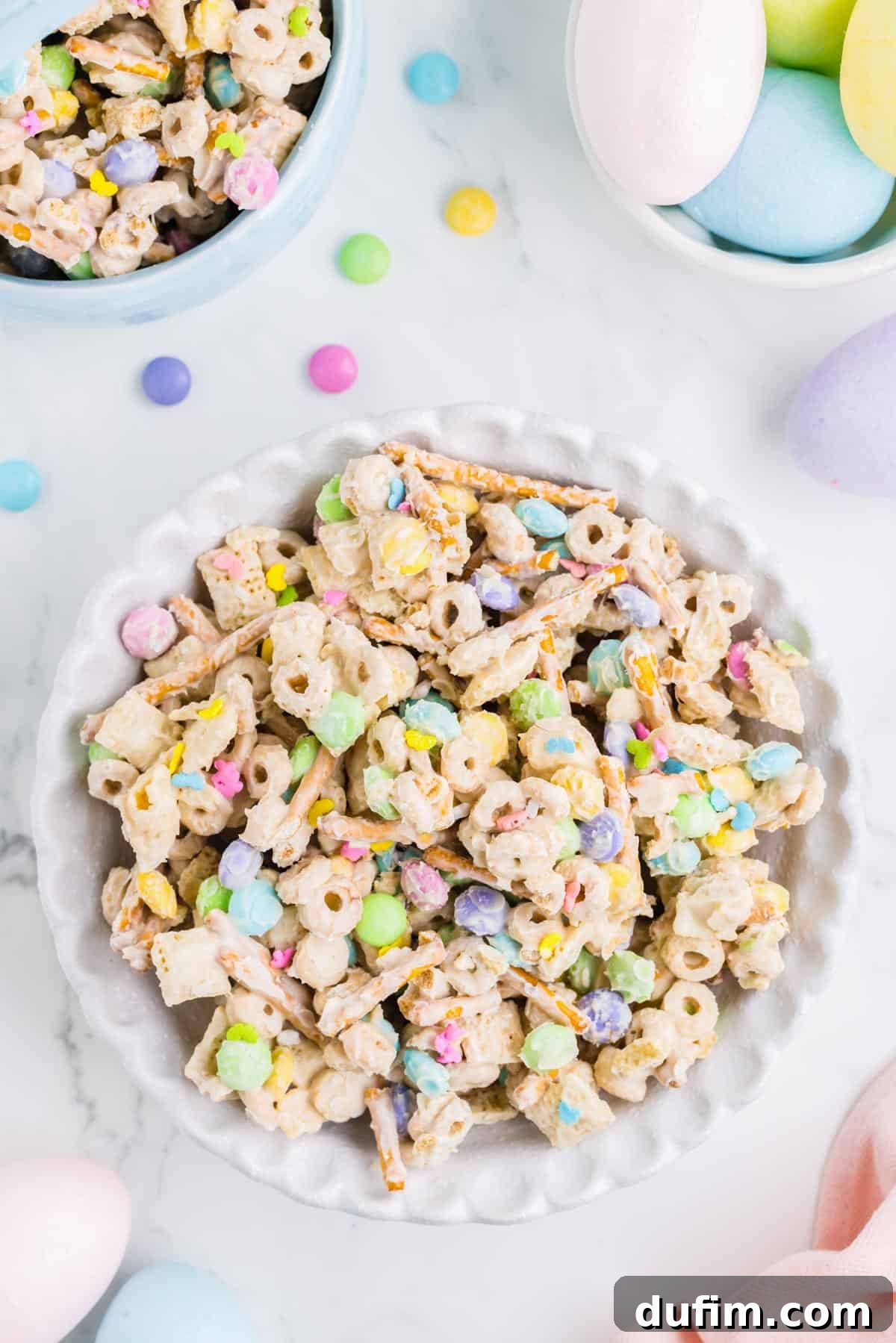 a large white bowl of bunny bait snack mix surrounded by a smaller bowl of bunny bait and a bowl of easter eggs