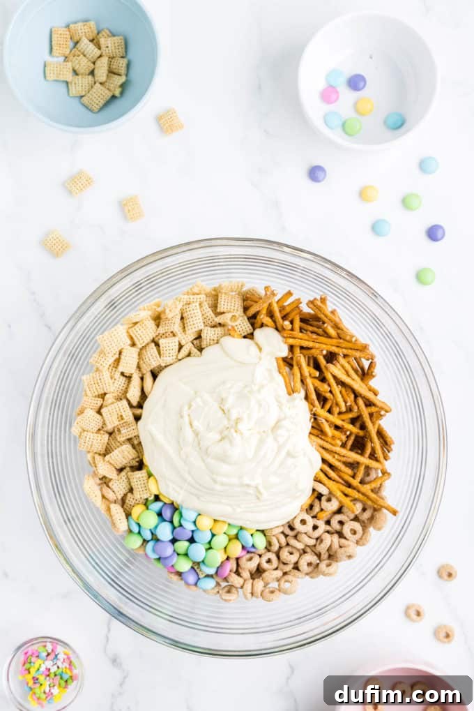 ingredients for bunny bait in a clear glass bowl surrounding by a bowl of sprinkles, a bowl with cheerios in it, a bowl of rice chex and a bowl of m&ms