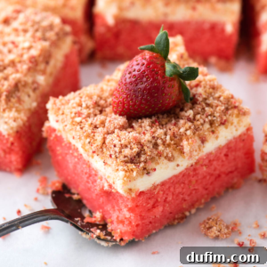 A delicious slice of Strawberry Crunch Cake with its vibrant pink cake, creamy white frosting, and golden strawberry crumble topping