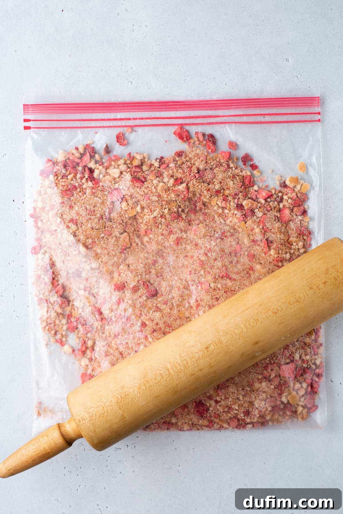 Crushed Nilla wafers and freeze dried strawberries in a ziploc bag with a rolling pin on top, showing the prepared topping