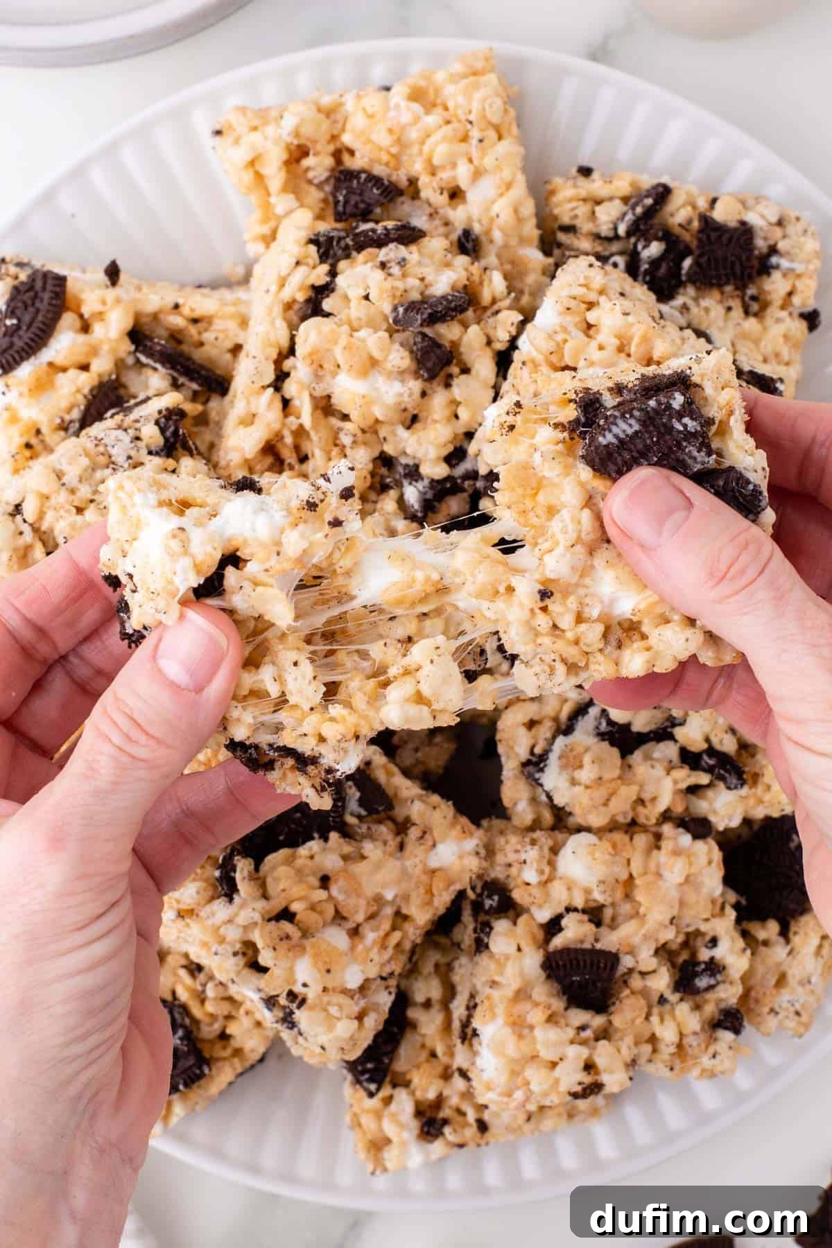 Oreo Dream Krispie Bars 2 two hands pulling apart a gooey oreo rice krispies treat above a plate full of more rice krispie treats