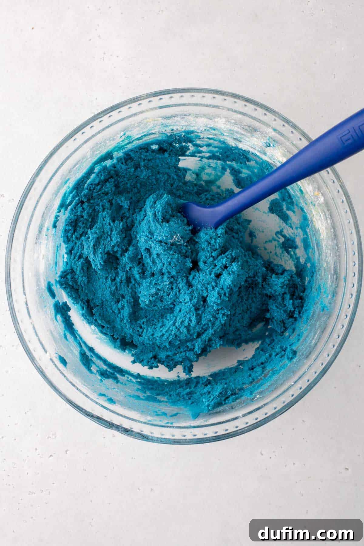 A glass mixing bowl filled with a generous amount of vibrant blue cookie dough, showcasing the perfect Cookie Monster hue before additional mix-ins are added.