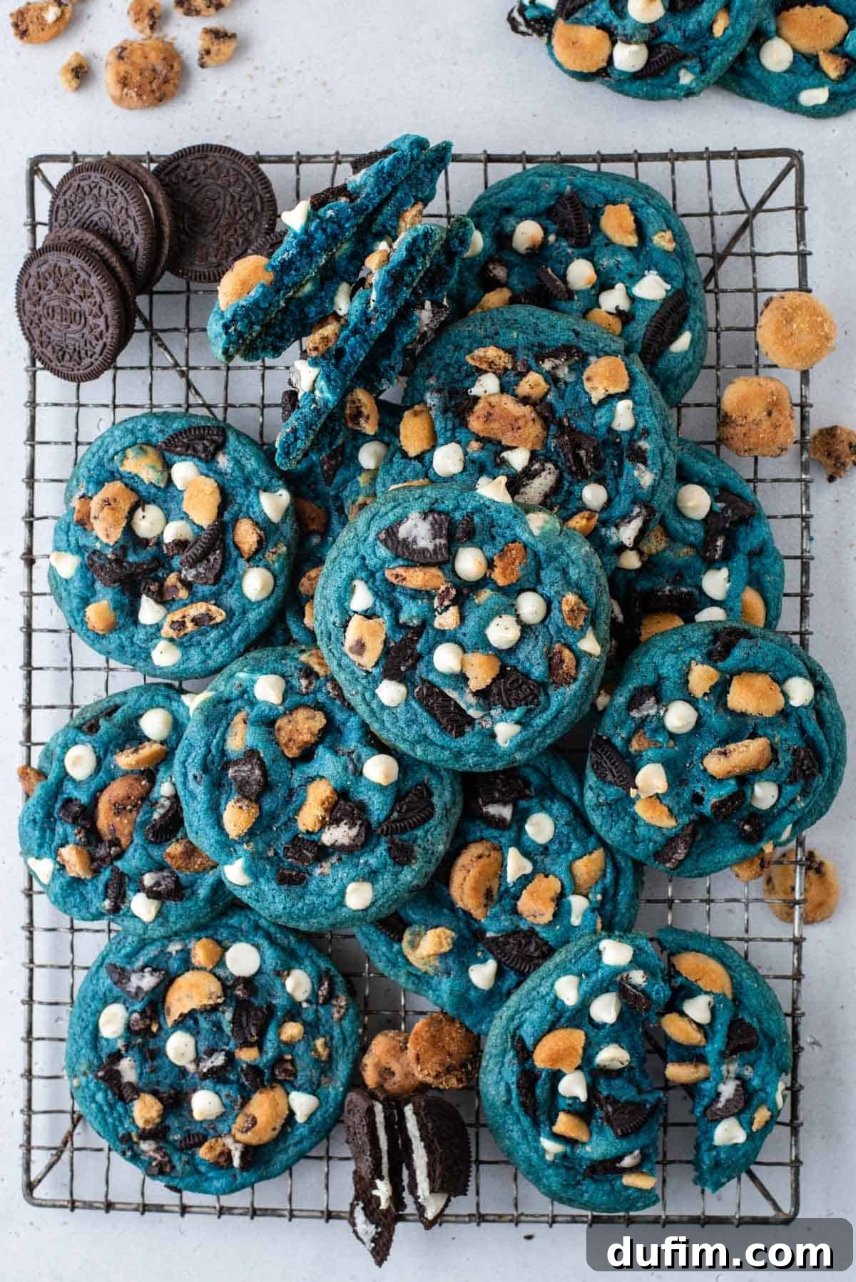 A generous pile of freshly baked Cookie Monster Cookies cooling on a wire rack. Mini Oreos and Chips Ahoy cookies are scattered around, emphasizing the fun mix-ins.