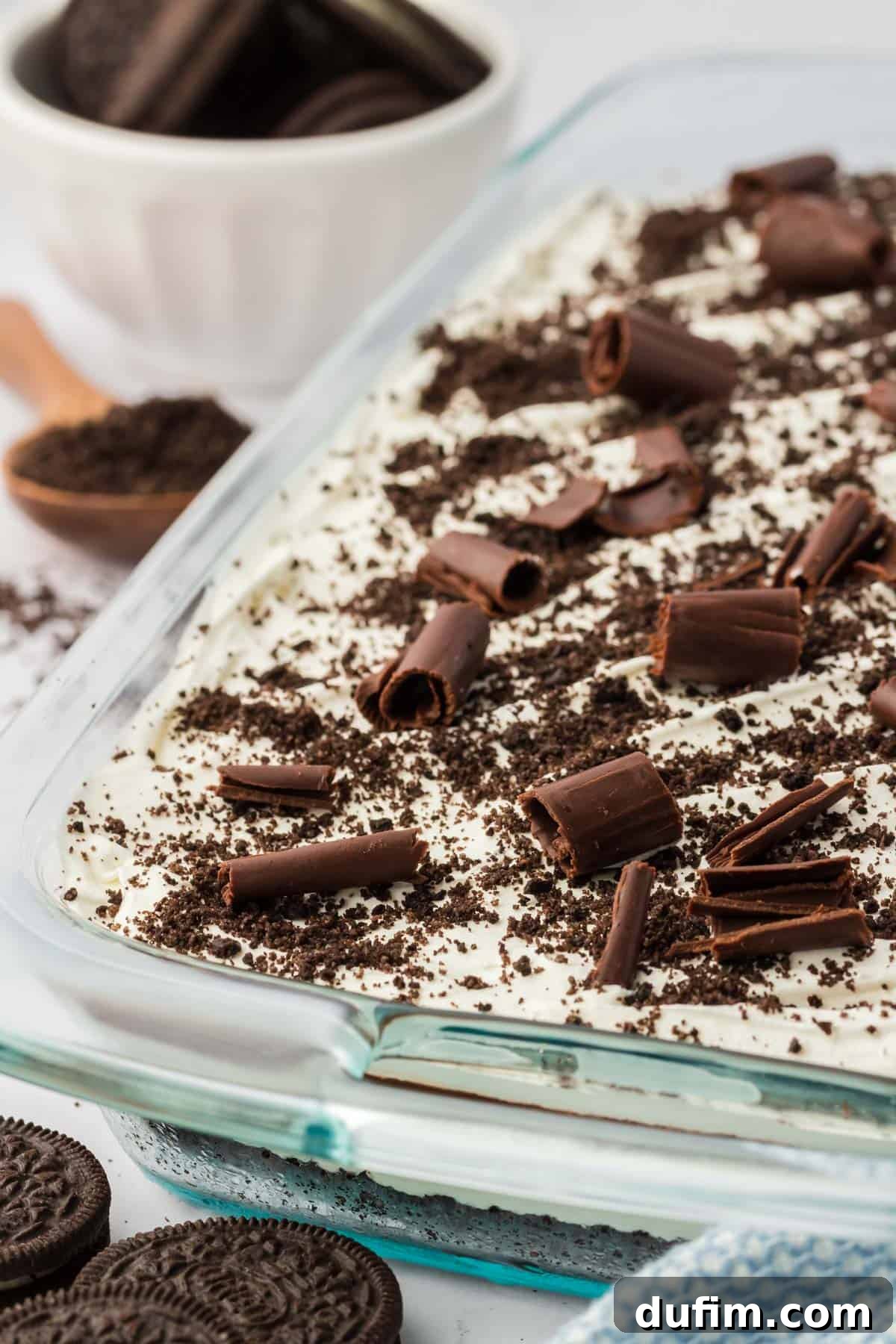 Ultimate Chocolate Lasagna Indulgence 8 A close-up of the top of a pan of chocolate lasagna, generously garnished with intricate chocolate shavings and scattered Oreo crumbs, surrounded by whole Oreo cookies and a spoonful of crumbs.
