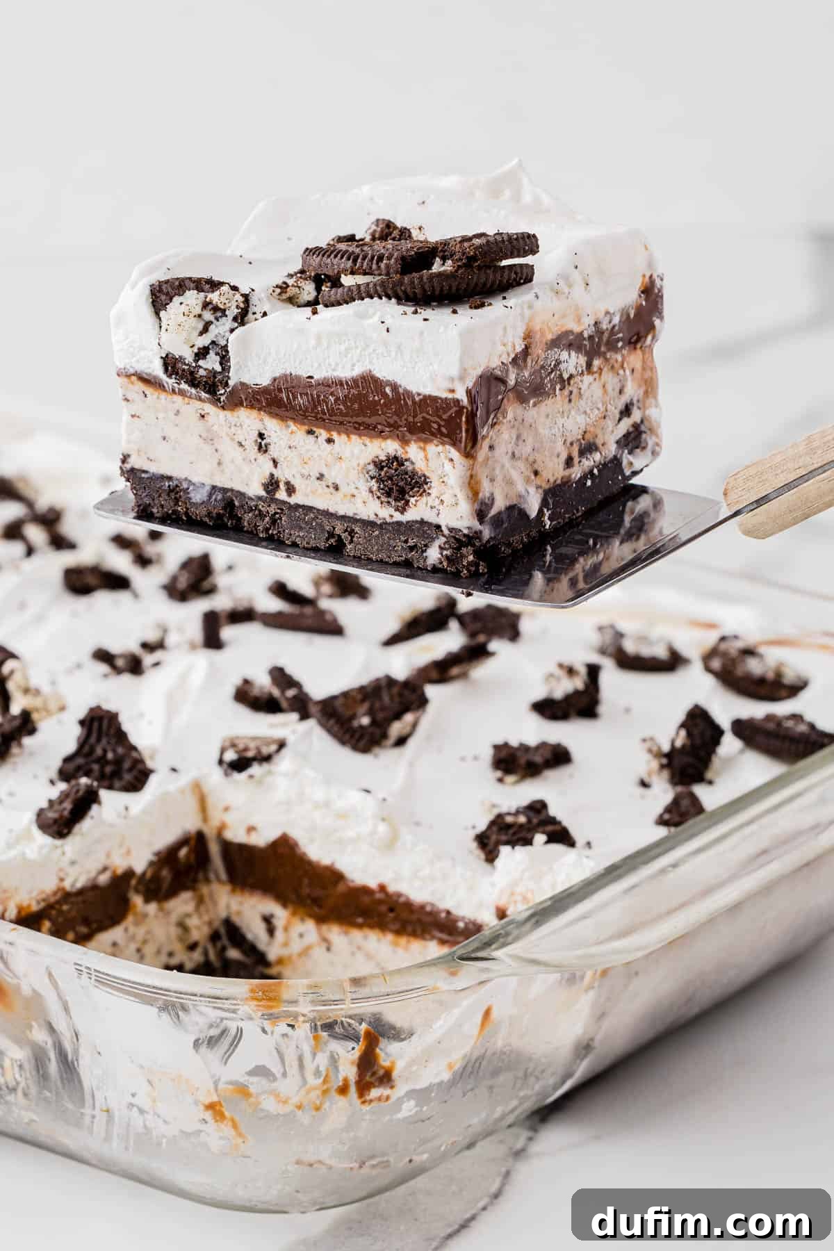 A slice of irresistible Oreo ice cream cake being carefully lifted from a serving dish with a spatula, highlighting its impressive height and delicious layers.