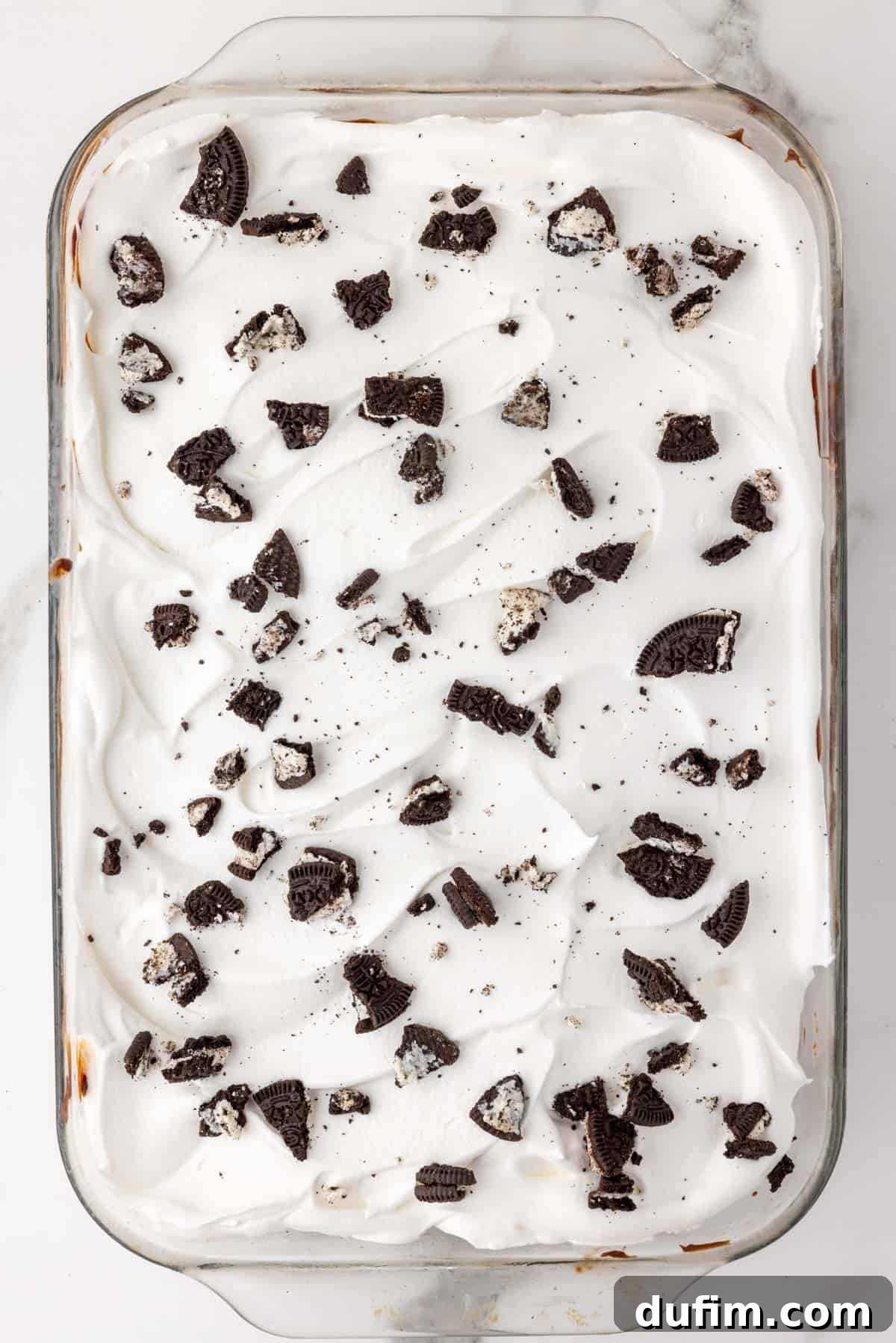 The finished top of the Oreo ice cream cake in a baking dish, generously garnished with extra crushed Oreo cookie pieces, ready for final freezing.