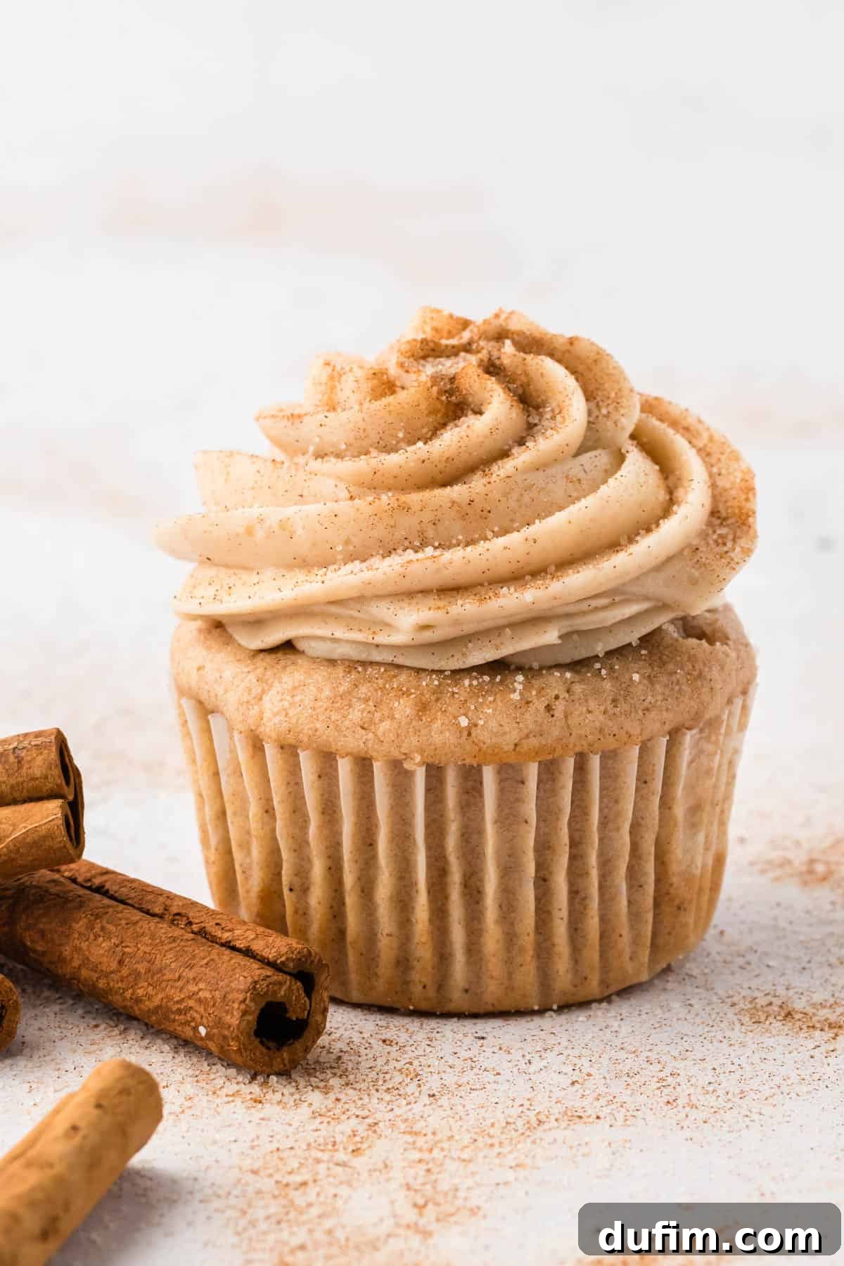 Dreamy Cinnamon Cream Cheese Frosting 2 Cinnamon cream cheese frosting piped elegantly on a muffin, surrounded by aromatic cinnamon sticks and dusted with cinnamon sugar, creating an inviting visual for a spiced dessert.