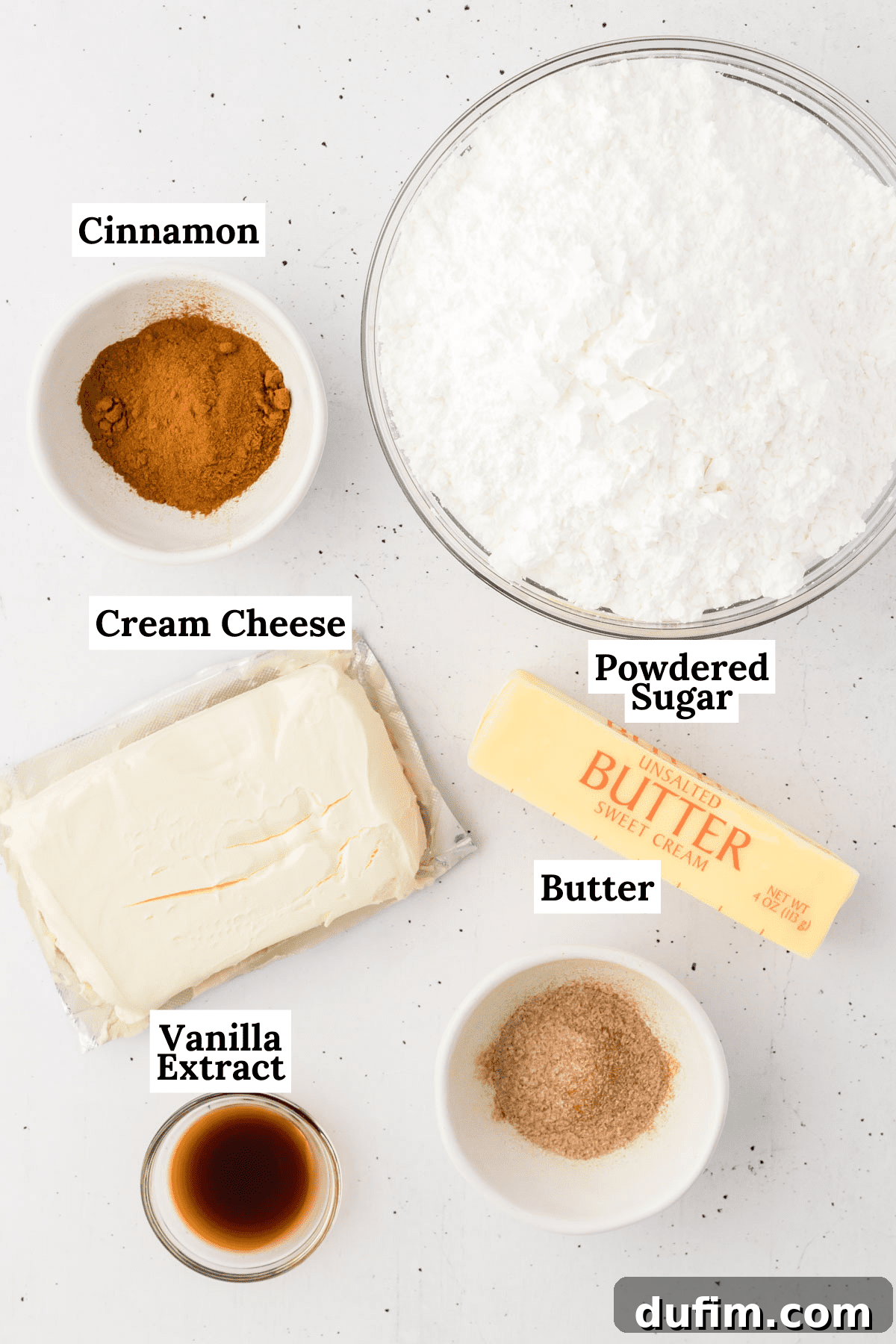 Dreamy Cinnamon Cream Cheese Frosting 4 A curated display of ingredients for cinnamon cream cheese frosting, including blocks of cream cheese and butter, a bowl of powdered sugar, a bottle of vanilla extract, a jar of ground cinnamon, and a small dish of cinnamon sugar, ready for mixing.