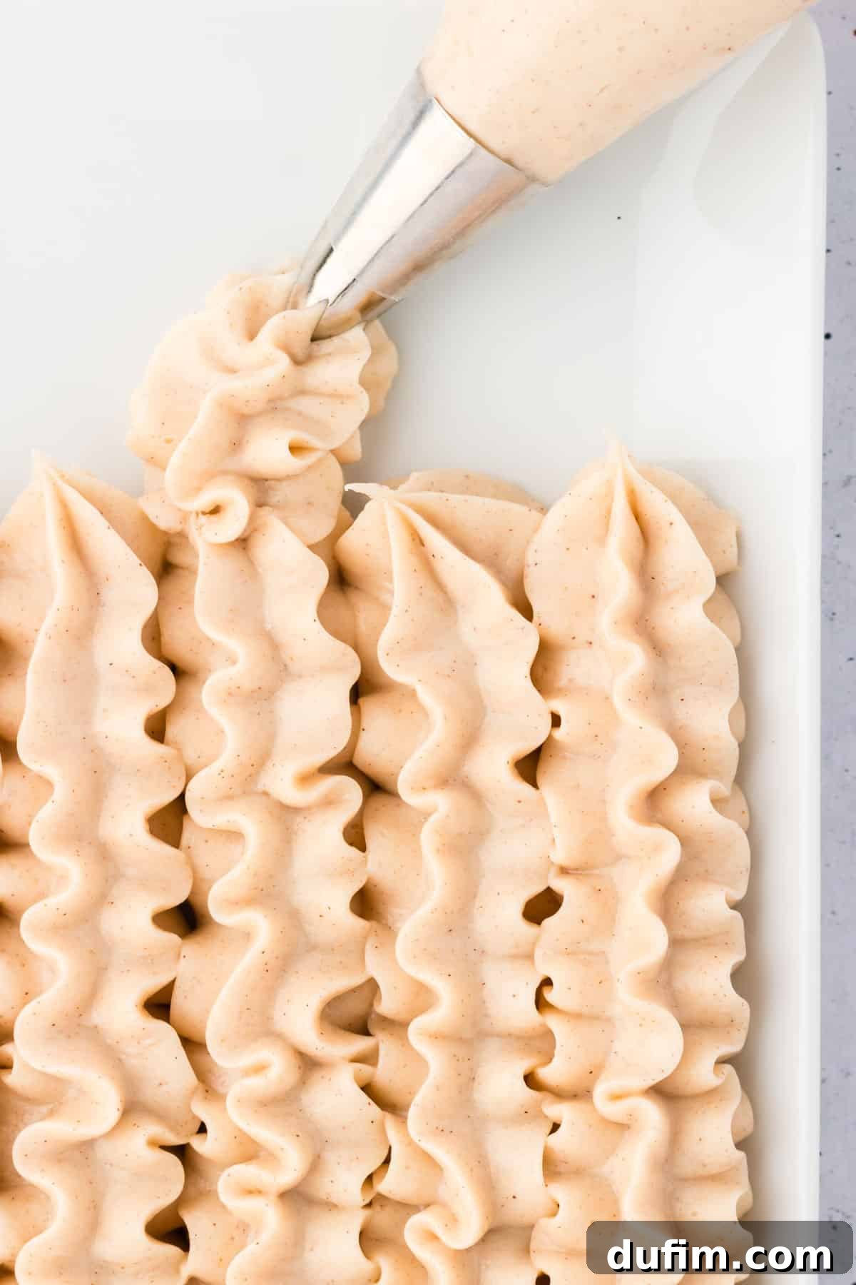 Dreamy Cinnamon Cream Cheese Frosting 5 A close-up view of cinnamon cream cheese frosting piped into neat lines in a pristine white dish, showcasing its smooth texture and readiness for use.