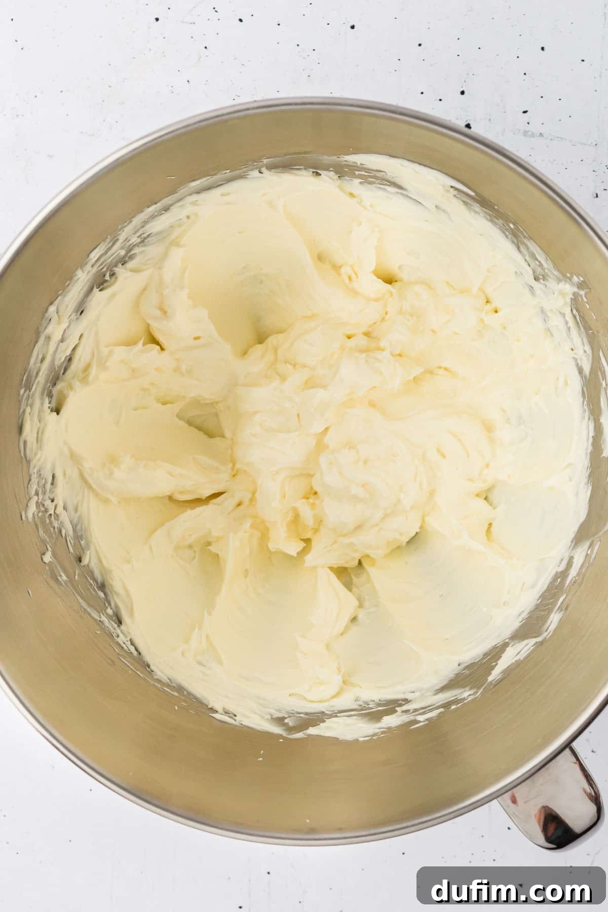 Dreamy Cinnamon Cream Cheese Frosting 6 The creamy base for cream cheese frosting, a mixture of butter and cream cheese, sits ready in a polished metal mixing bowl, showcasing its smooth texture before other ingredients are added.
