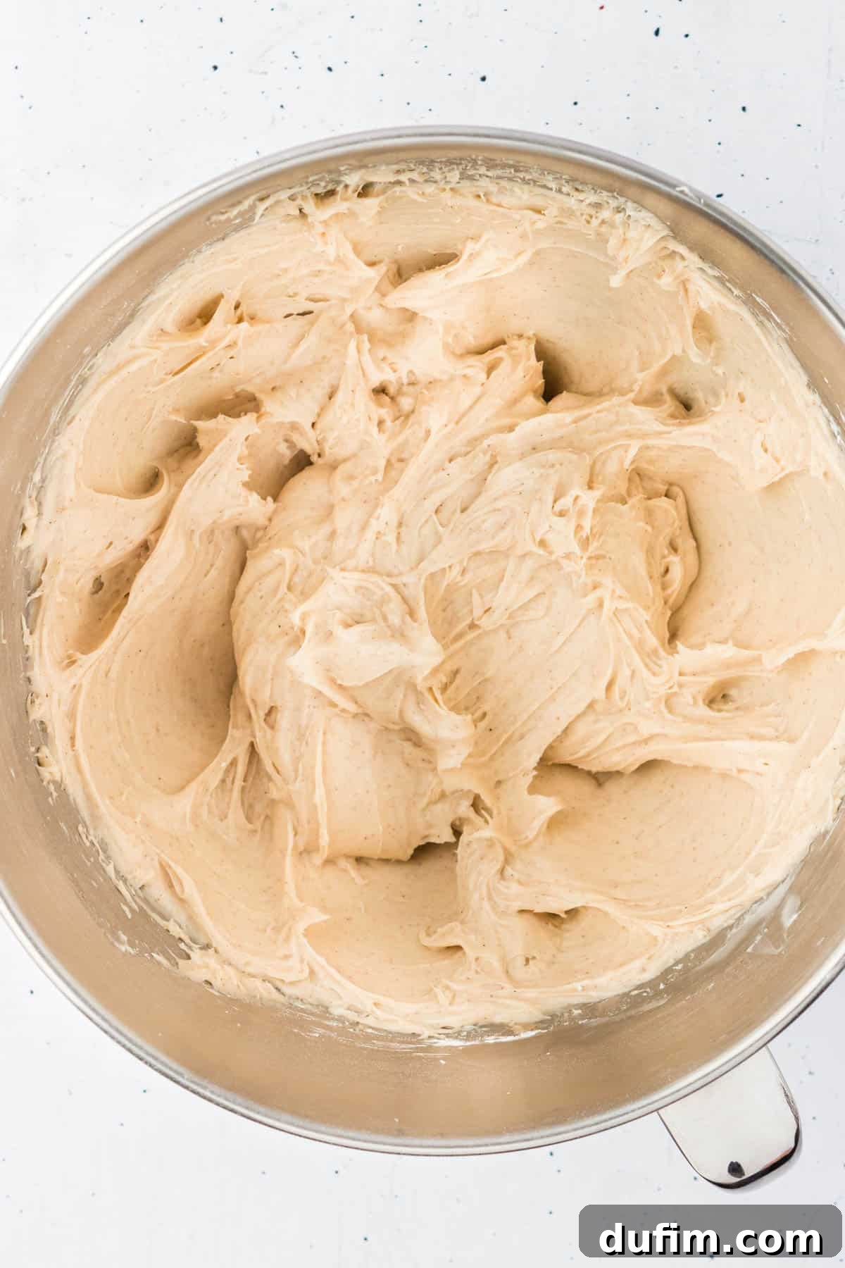Dreamy Cinnamon Cream Cheese Frosting 7 Freshly combined cinnamon cream cheese frosting, smooth and fluffy, fills a large mixing bowl, showing its readiness for application on various desserts.