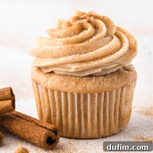 Cinnamon cream cheese frosting on top of a cupcake with cinnamon sticks beside it