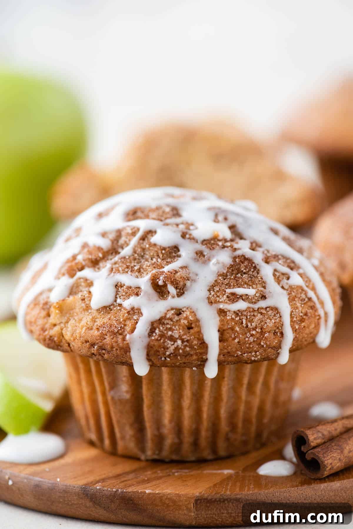 Tender Apple Cinnamon Treats 2 A perfectly baked apple cinnamon muffin on a rustic wooden platter, artfully arranged with cinnamon sticks and fresh apple slices, highlighting its moist texture and rich flavors.