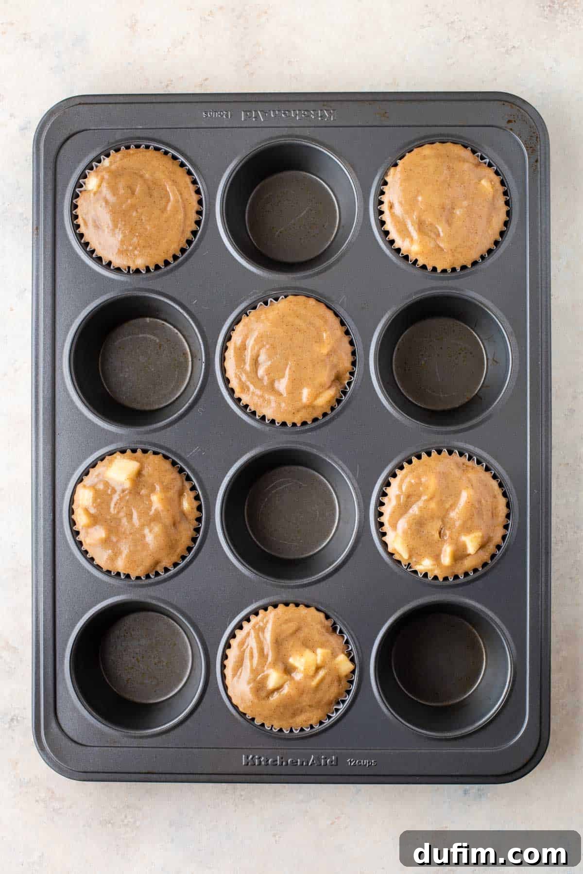 Tender Apple Cinnamon Treats 7 A muffin pan thoughtfully arranged with apple cinnamon muffin batter in every other muffin well, demonstrating the strategic spacing for optimal bakery-style dome formation.