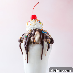 a hot fudge sundae topped with peanuts, sprinkles and a cherry on top against a pink background