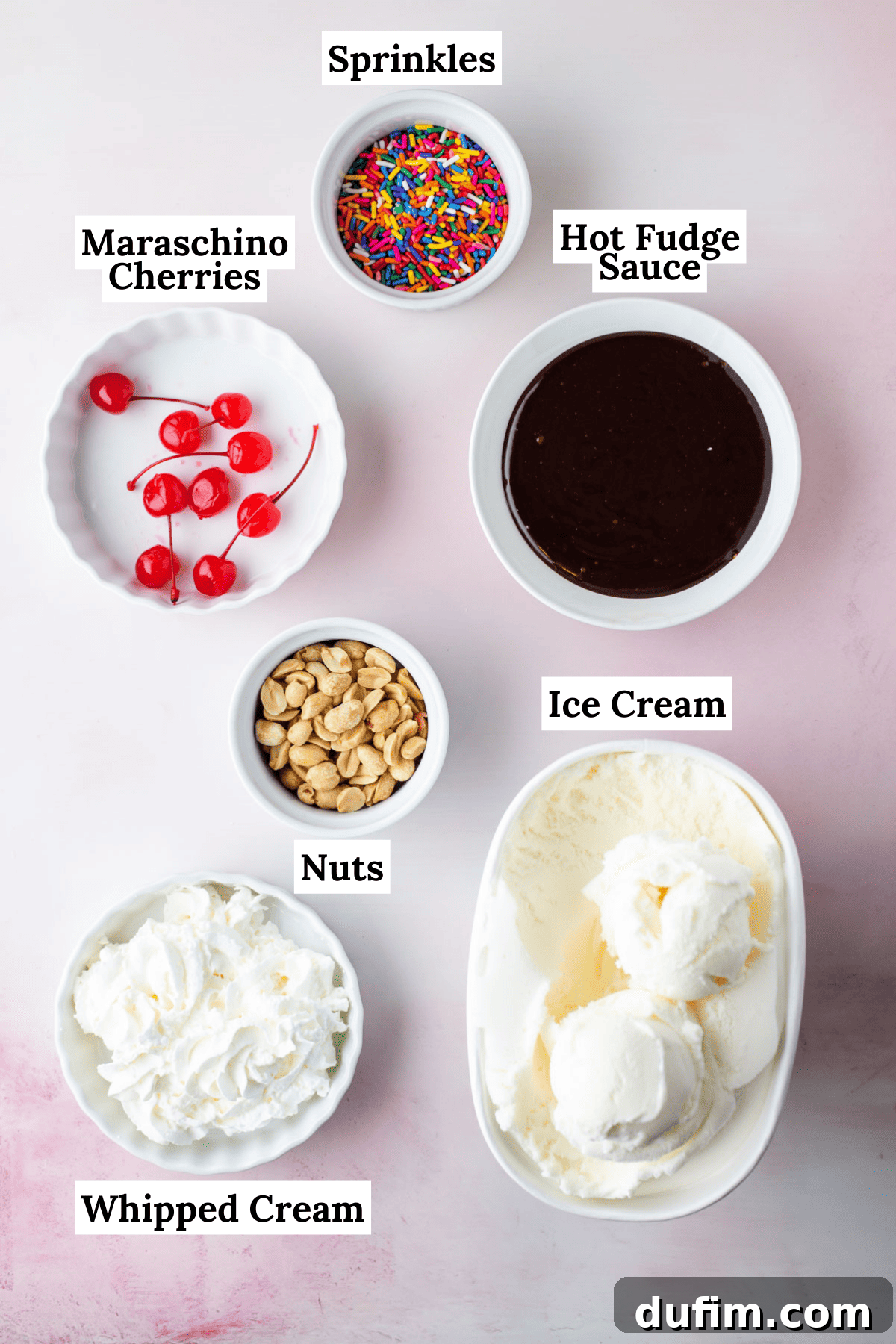 the ingredients for a hot fudge sundae laid out including a bowl of sprinkles, a bowl of hot fudge sauce, a bowl of maraschino cherries, a bowl of peanuts, a bowl of whipped cream and a bowl of vanilla ice cream