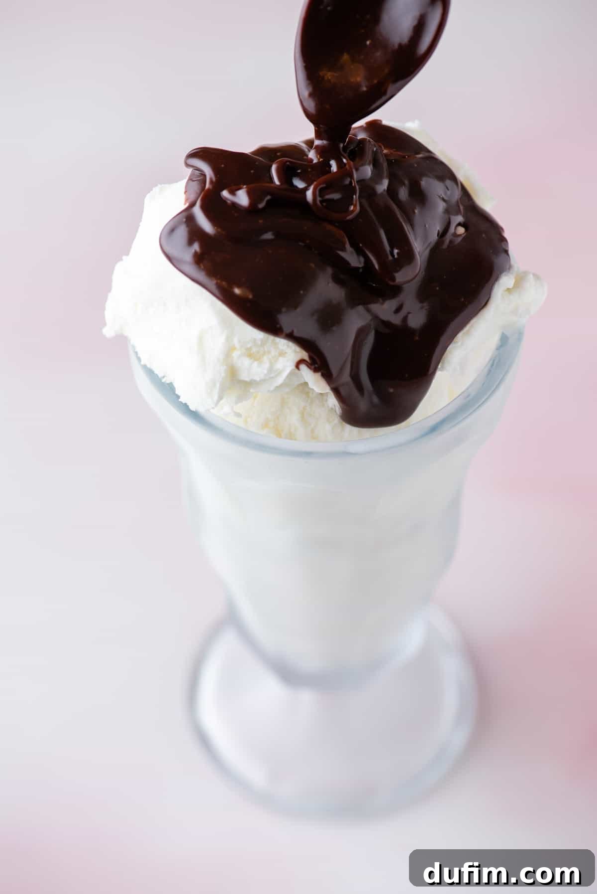 a tall glass filled with vanilla ice cream being topped with hot fudge sauce