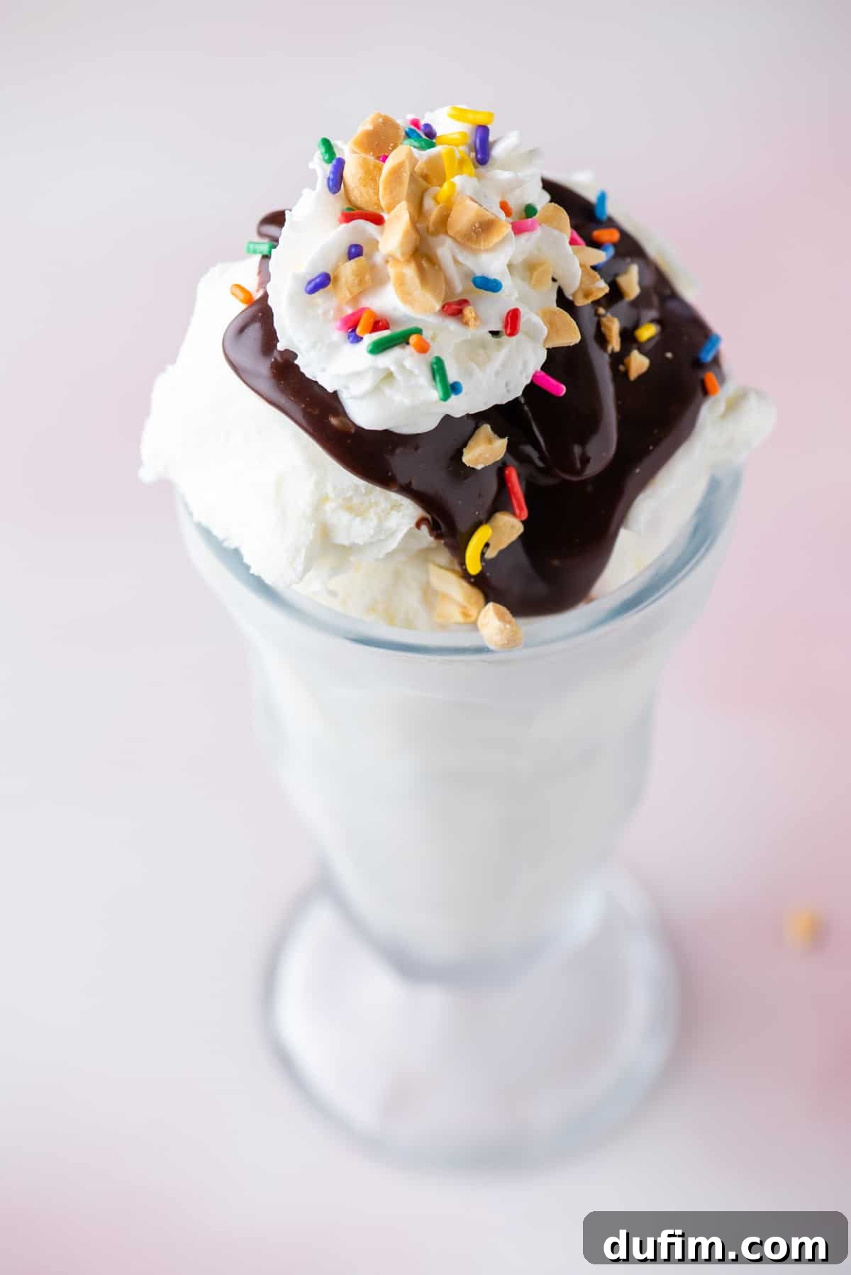 a hot fudge sundae in a tall glass topped with sprinkles, peanuts and cool whip