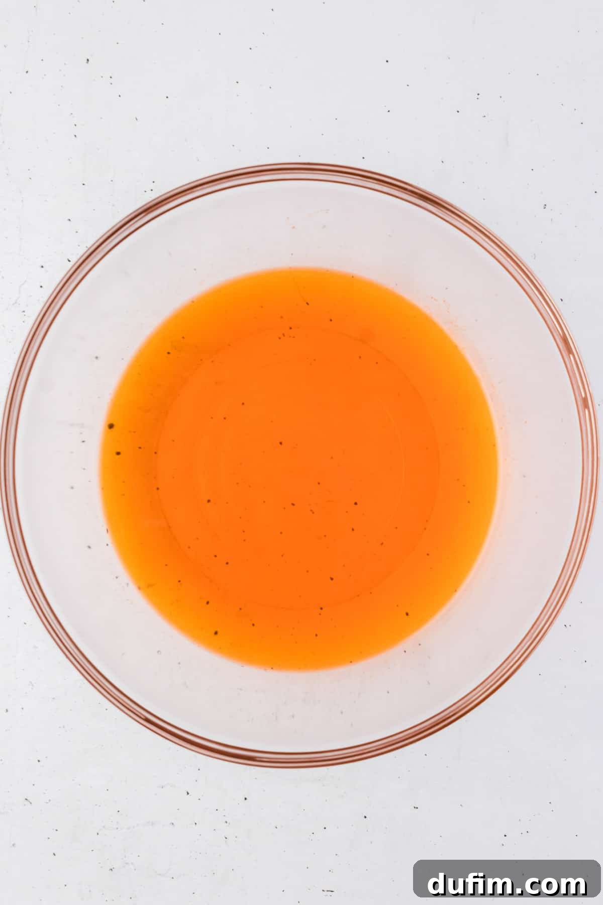 A vibrant heap of orange jello mix powder resting in the bottom of a clear glass mixing bowl, poised for preparation. This image captures the initial step of combining the dry ingredients, suggesting the start of a sweet culinary adventure.