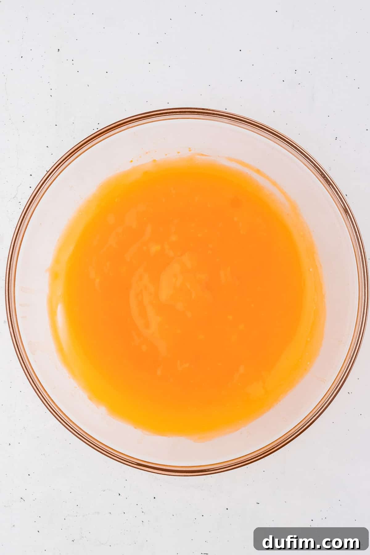 Orange jello mix powder meticulously combined with water in a clear glass mixing bowl, the liquid a translucent, glowing orange. This visual indicates the first stage of dissolving the jello, showing a smooth and well-mixed solution.
