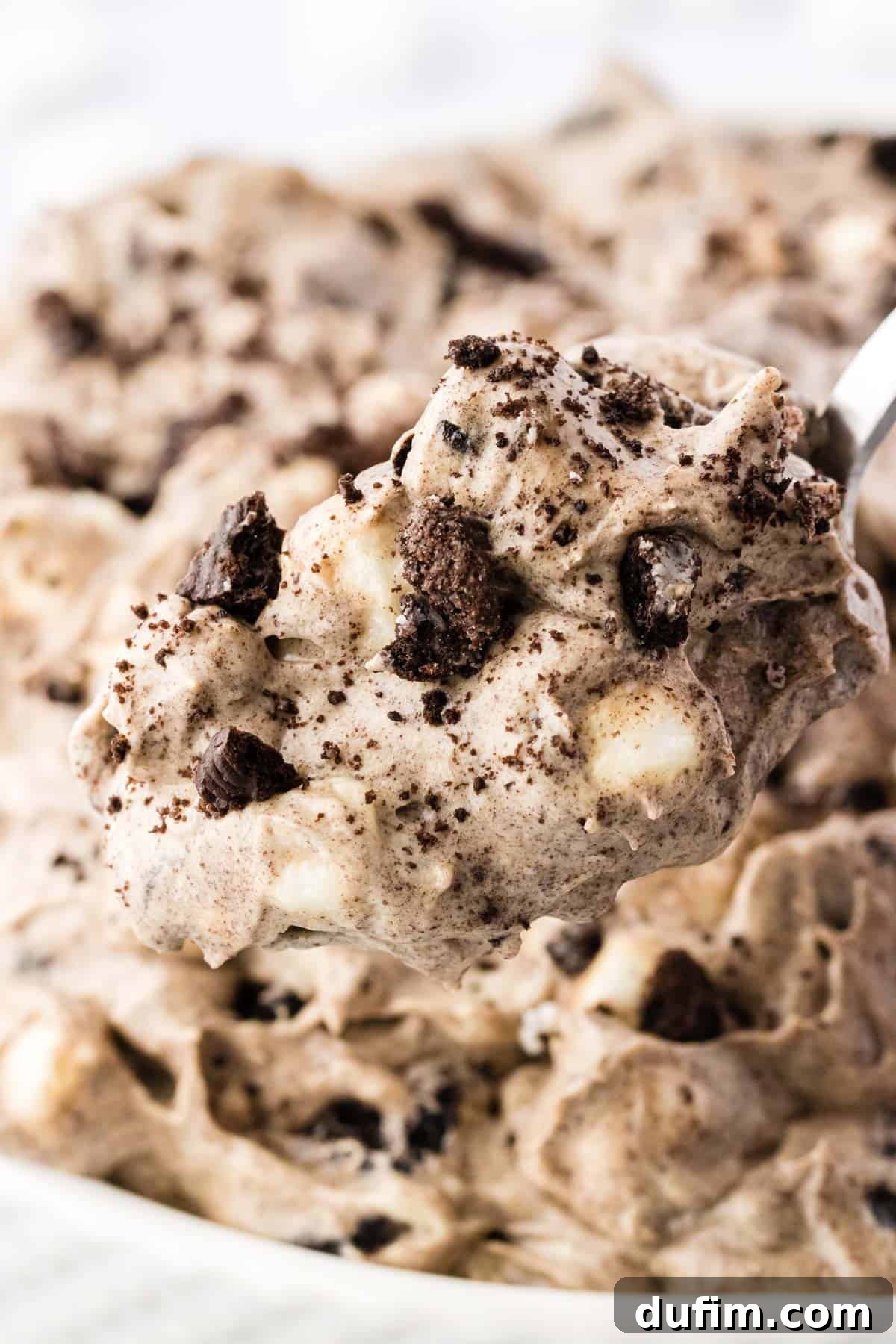 No-Fuss Oreo Fluff 11 A captivating close-up of a spoonful of Oreo fluff, being gently lifted from a bowl filled with the creamy dessert, highlighting its delectable texture and inviting appeal.
