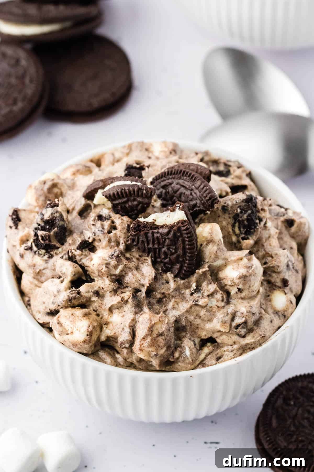 No-Fuss Oreo Fluff 13 Another enticing shot of Oreo fluff in a white bowl, artfully arranged with whole Oreo cookies, mini marshmallows, and a black and white checkered kitchen towel, emphasizing its dessert-ready presentation.