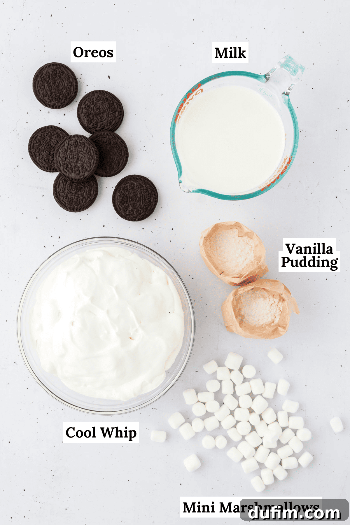 No-Fuss Oreo Fluff 4 All the essential ingredients for creating a delicious Oreo fluff laid out on a clean white surface: a box of vanilla pudding mix, a bottle of fresh milk, a container of cool whip, a package of classic Oreos, and a bag of mini marshmallows.
