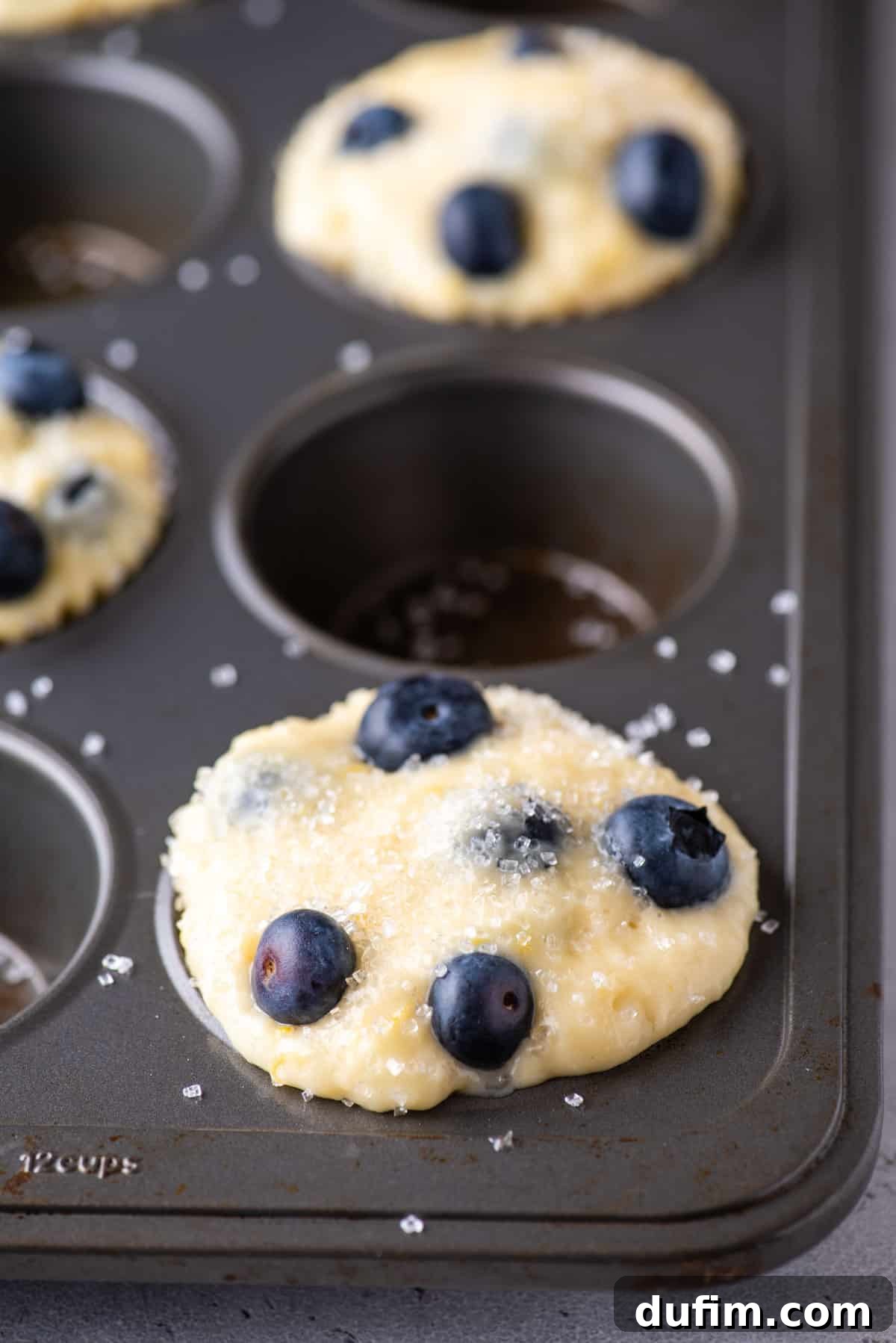Lemon blueberry muffin batter in a muffin pan, showing every other well filled.