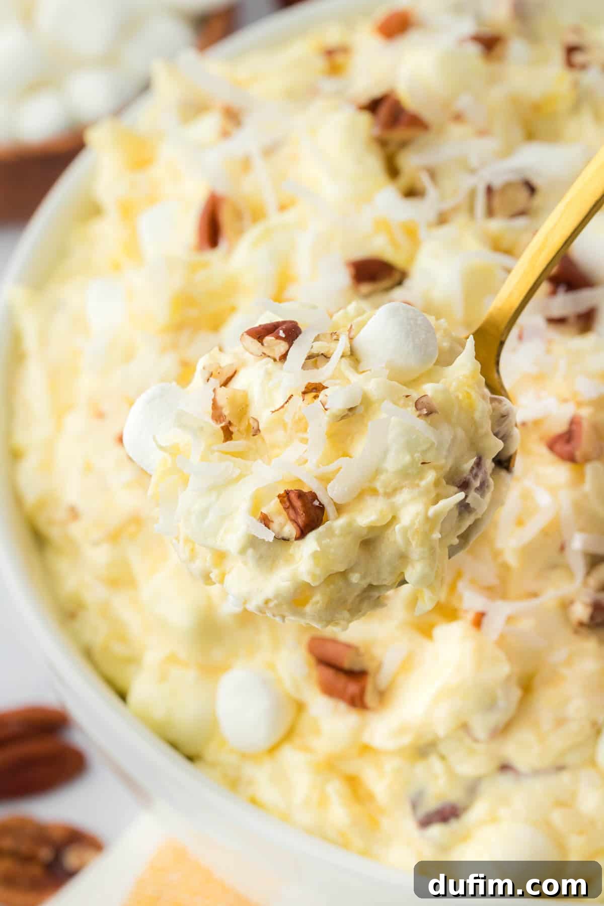 A spoon lifting a portion of creamy pineapple fluff from a large serving bowl, showcasing its delightful texture.