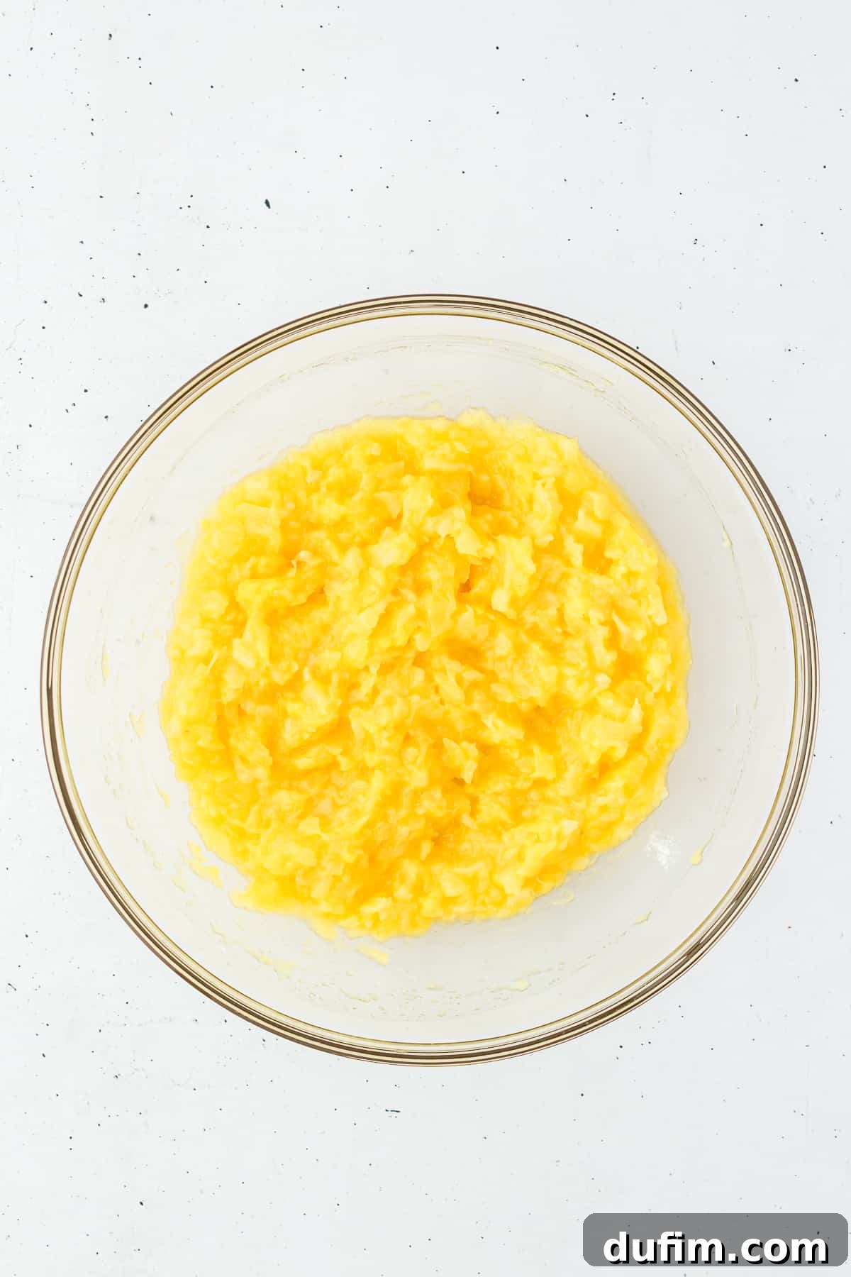 Crushed pineapple thoroughly mixed with vanilla pudding in a clear glass bowl, creating a smooth, vibrant base for the fluff.