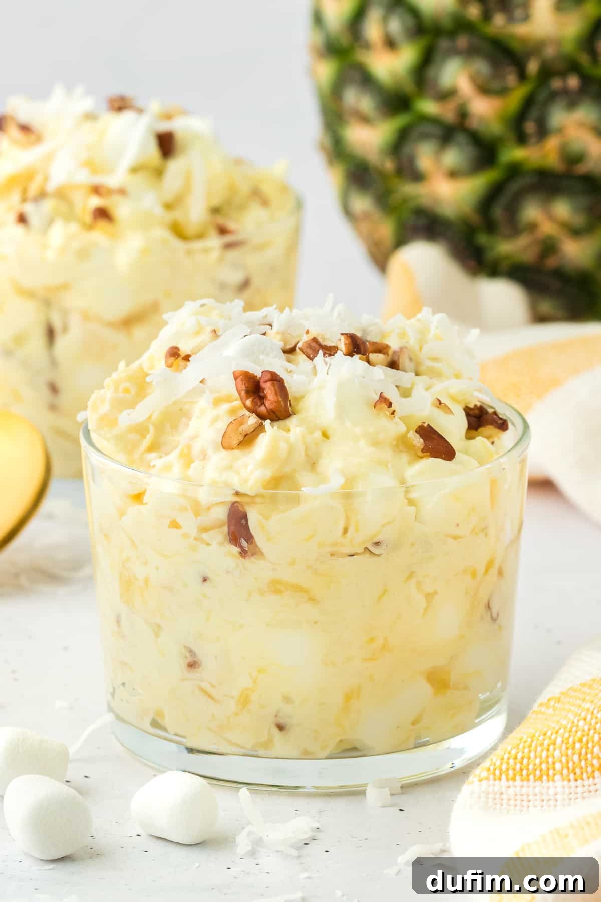 Two elegant clear trifle dishes, each filled with rich pineapple fluff, beautifully garnished with a scattering of nuts, mini marshmallows, and shredded coconut, emphasizing their readiness for serving.
