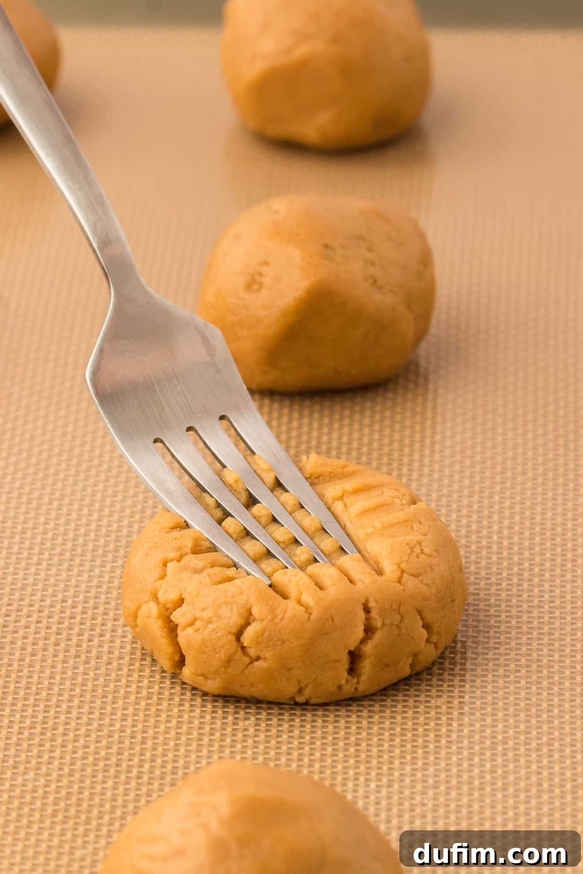 a fork creating a cross hatch pattern on gluten free peanut butter cookie dough balls on a baking sheet