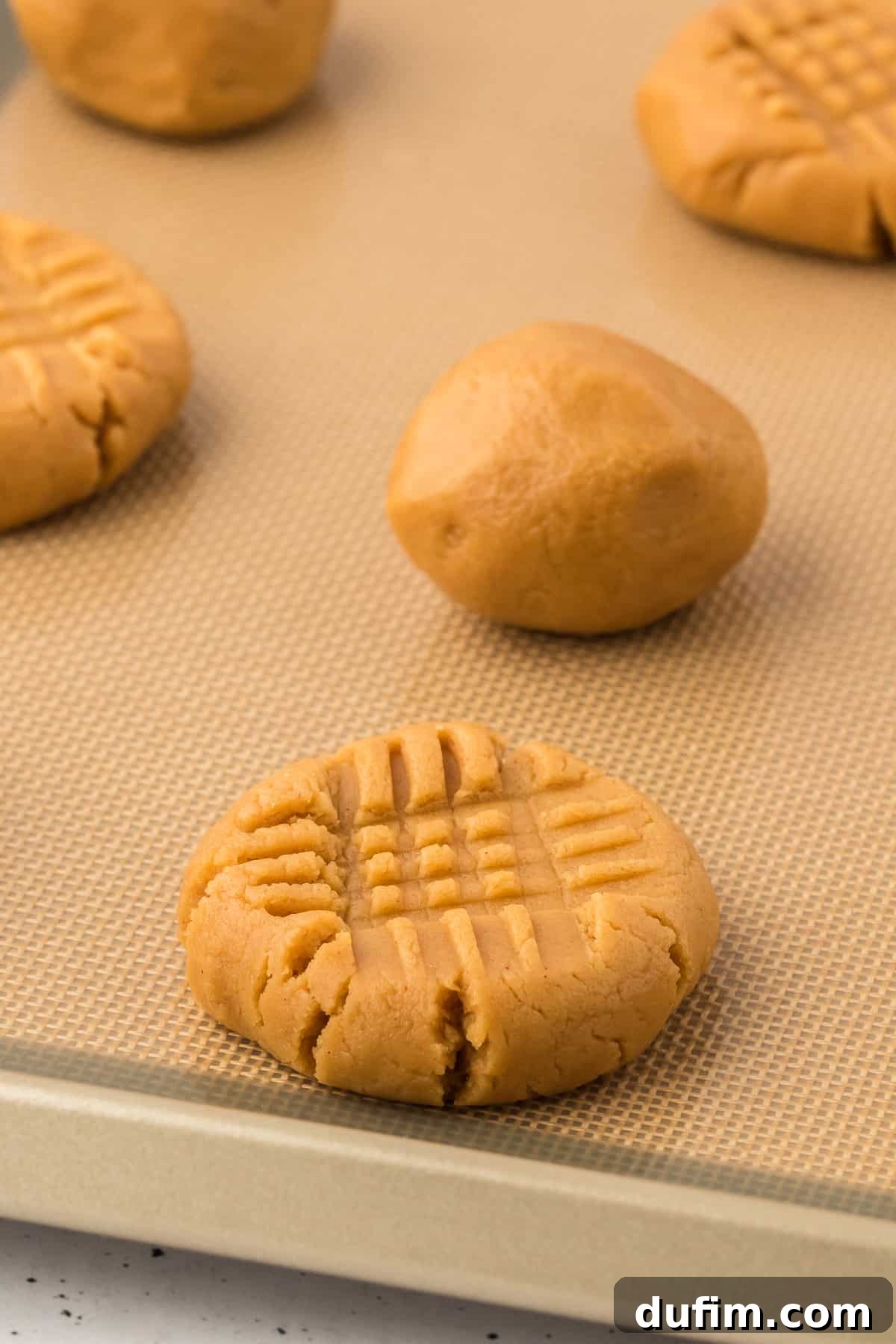 gluten free peanut butter cookie dough balls on a lined baking sheet, some pressed down into a cross hatch pattern and some still in ball form