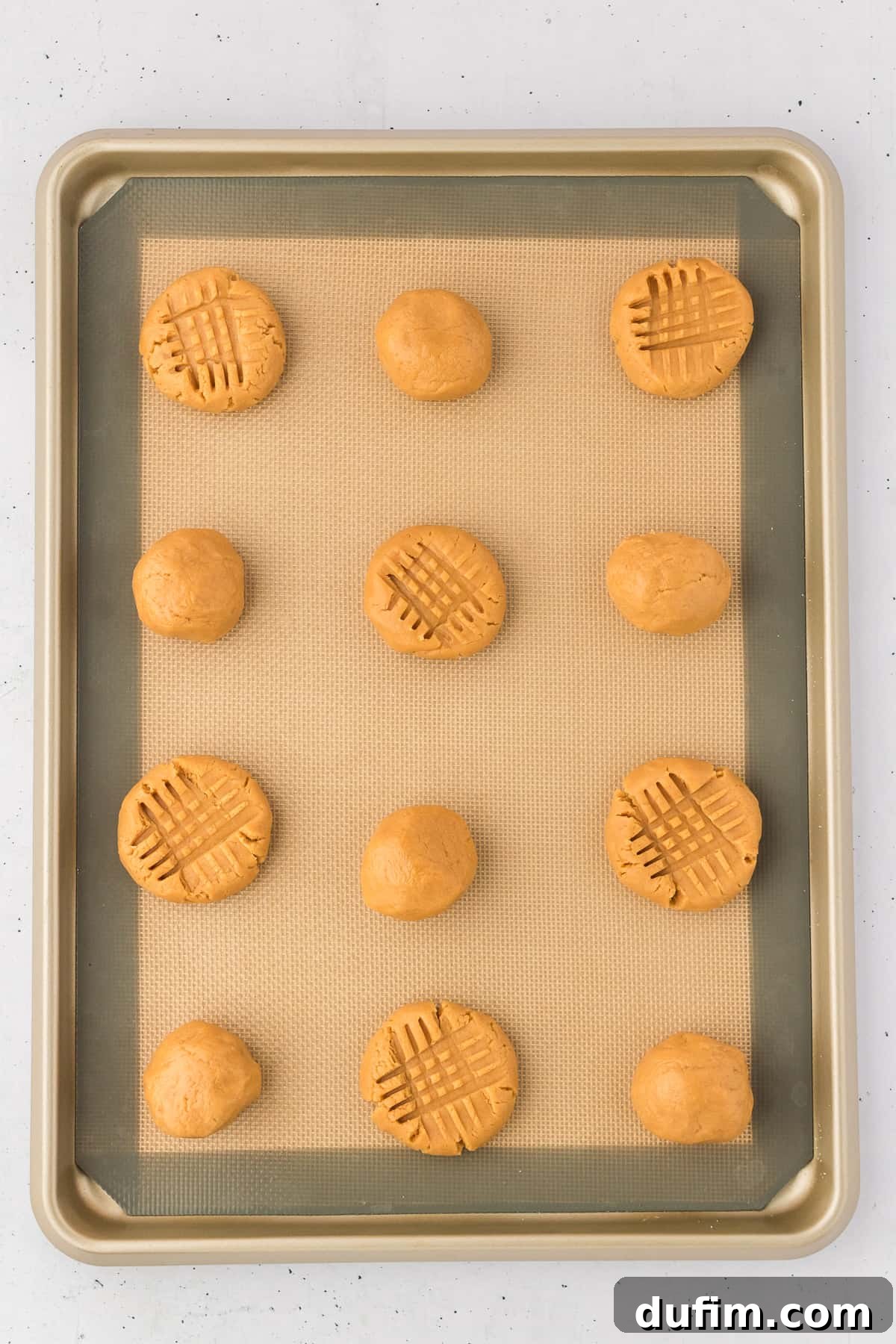 gluten free peanut butter cookie dough balls on a lined baking sheet, some pressed down into a cross hatch pattern and some still in ball form