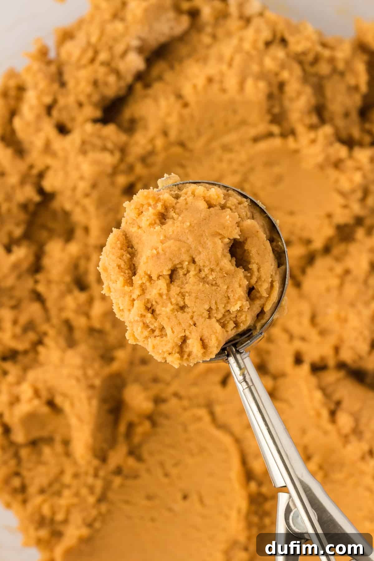a cookie scoop full of gluten free peanut butter cookie dough over of a bowl of cookie dough