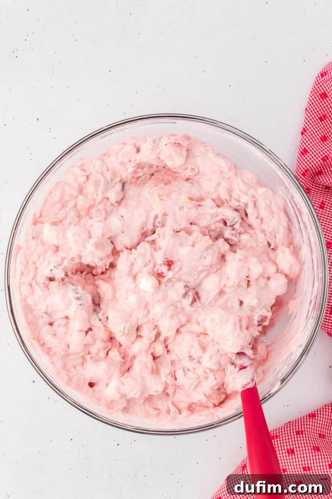 Cherry Fluff in a glass bowl with a red spatula stuck in it and a red and white kitchen towel to the right of it.