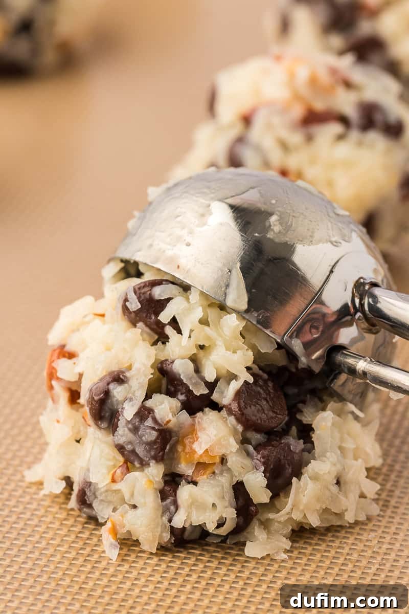 a cookie scoop placing a ball of almond joy cookie mixture on a silicone baking mat