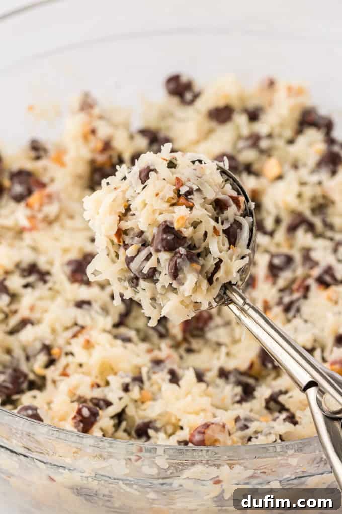 Cookie scooper full of almond joy cookie mixture over top of a bowl of the mixture